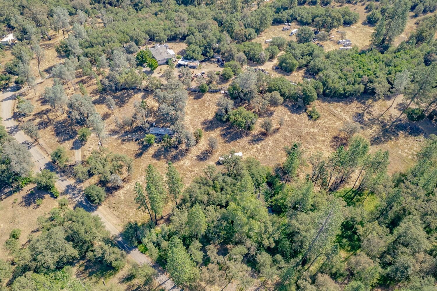 Aerial view of a rural property with scattered homes, outbuildings, trees, and open dry fields.