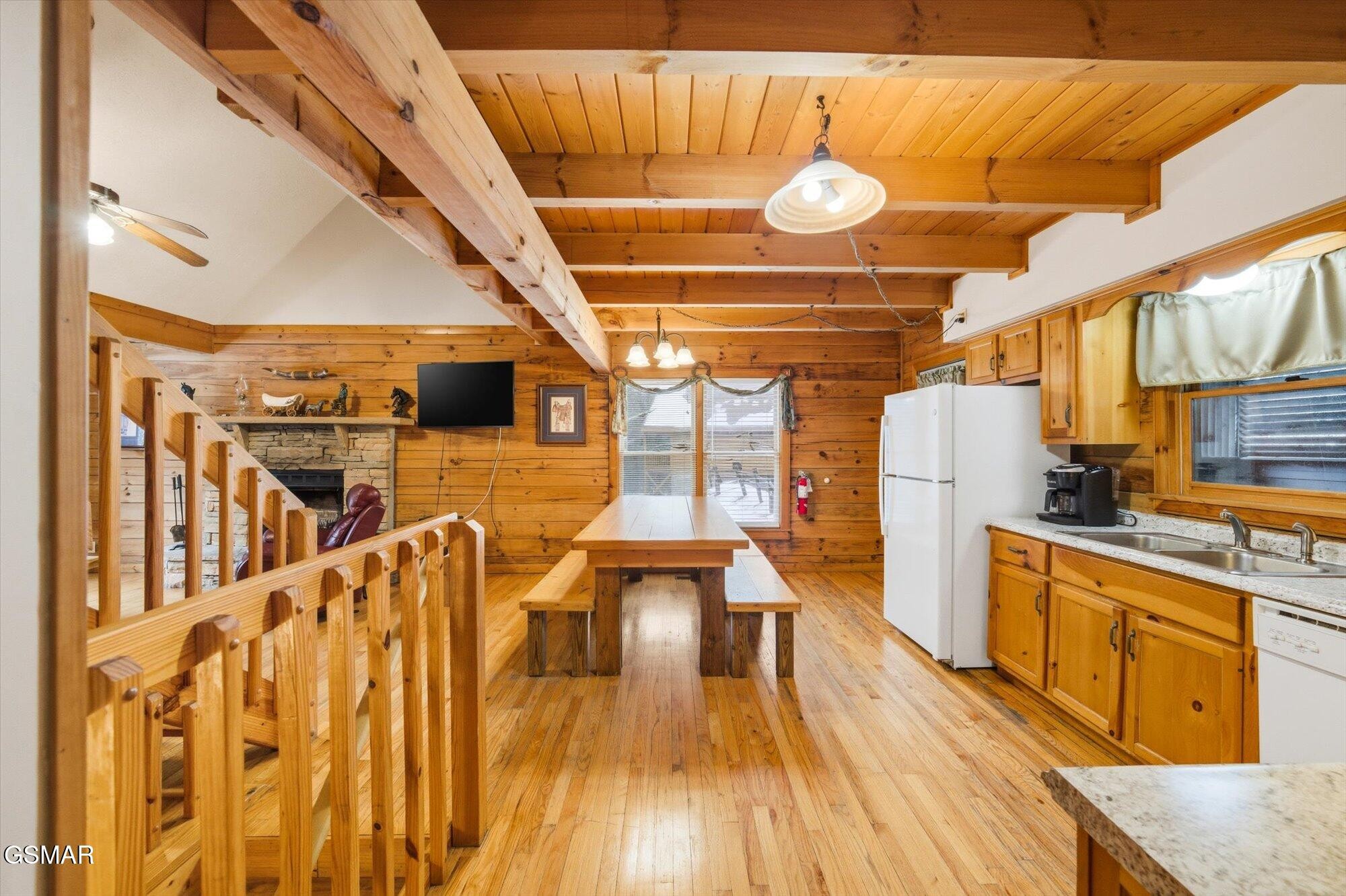 Rustic cabin kitchen and dining area with exposed timber beams, a long table, and a stone fireplace.