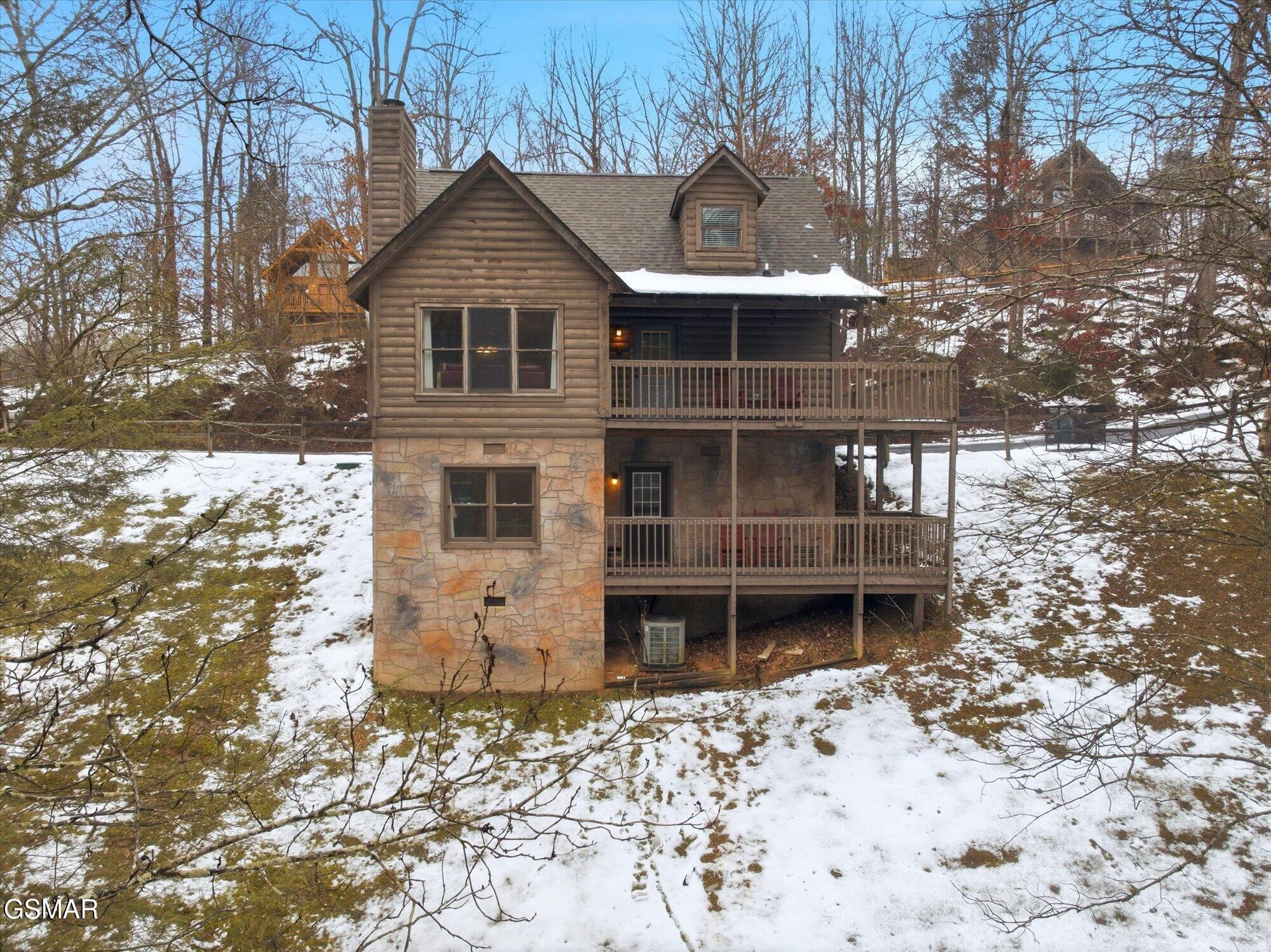Log cabin with two-level decks on a snowy wooded slope.