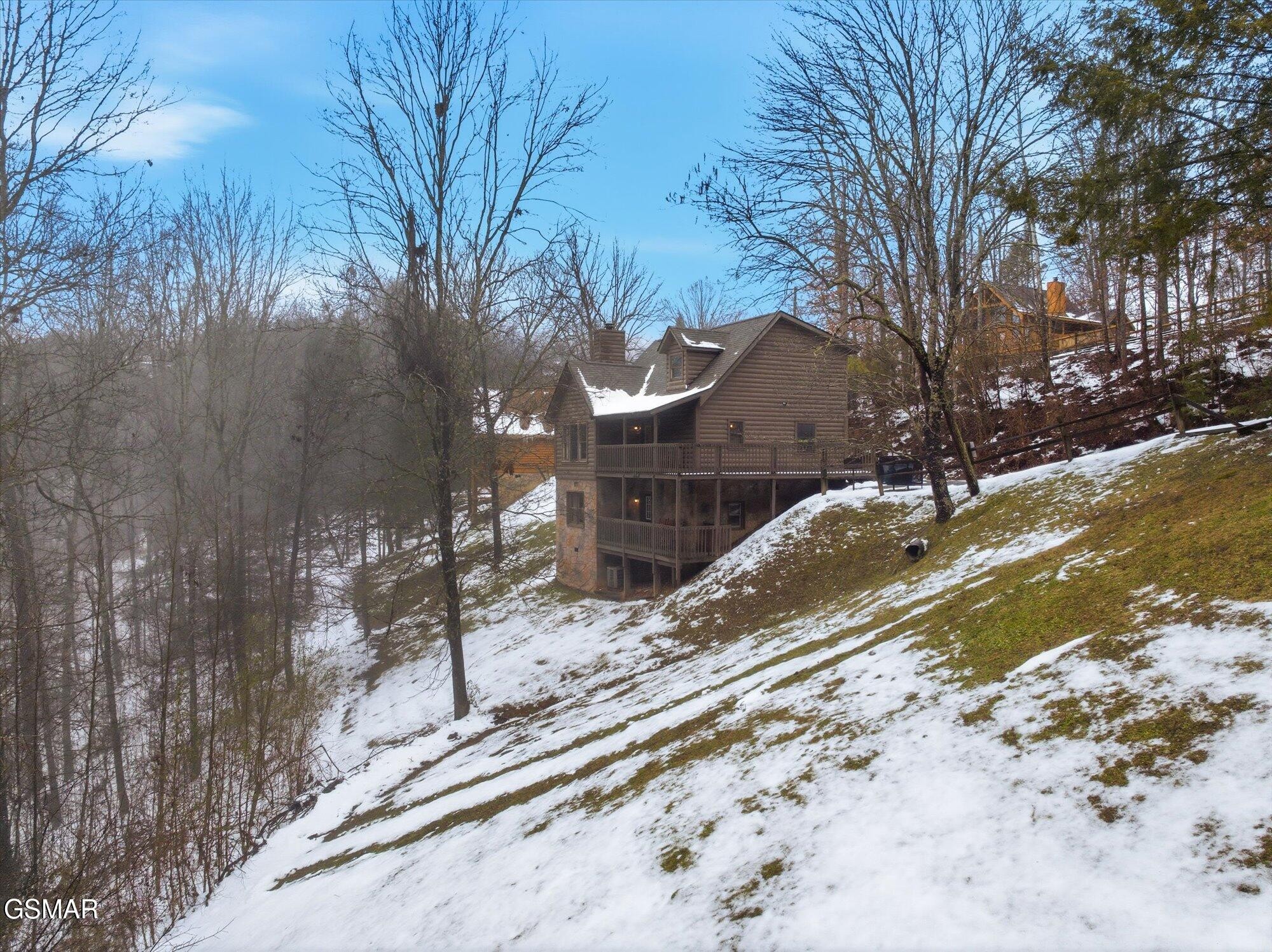Multi-level log cabin with covered decks on a snowy wooded hillside.