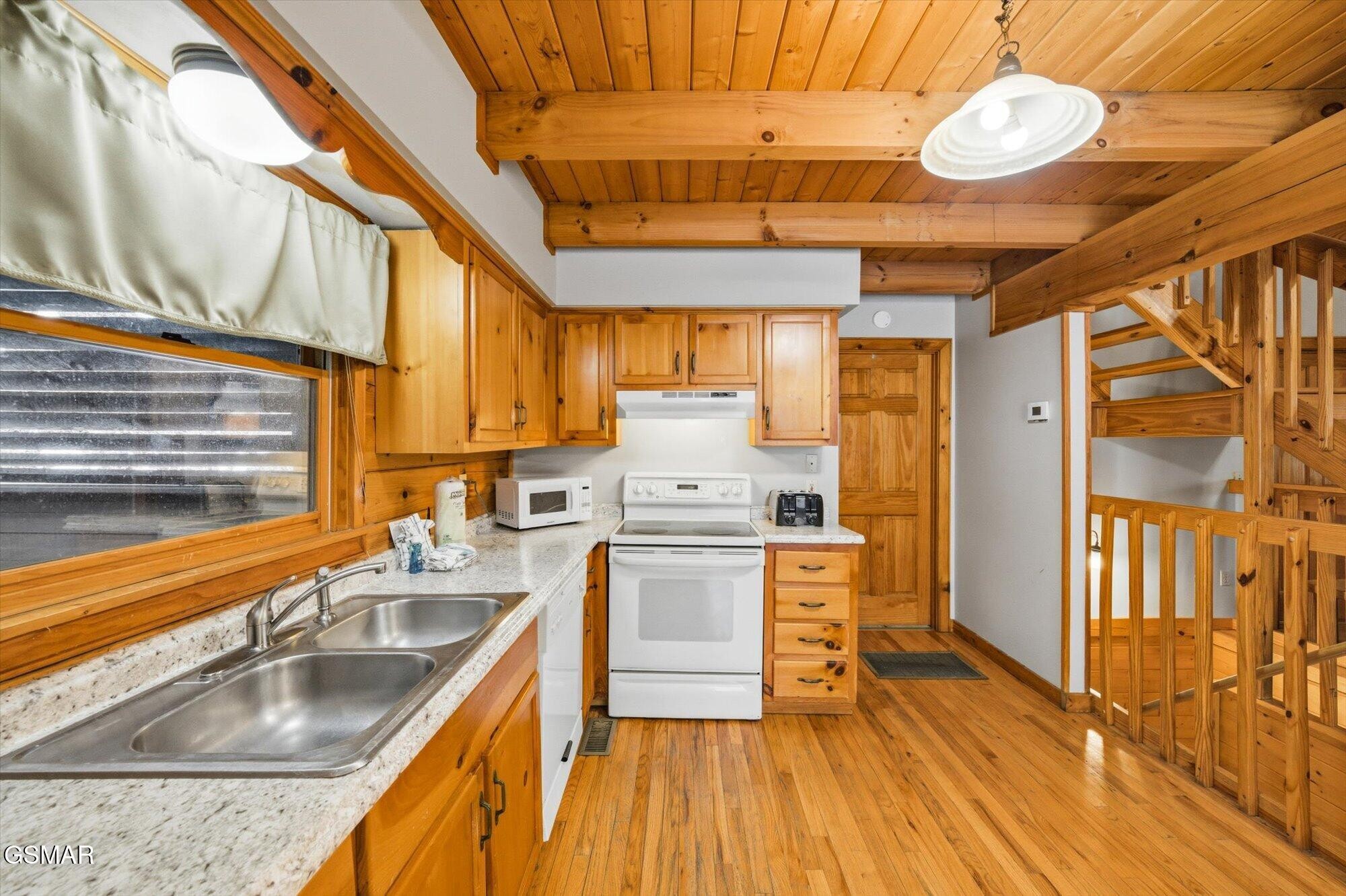 Cabin kitchen with wood cabinets, exposed ceiling beams, a double sink, and an open staircase.