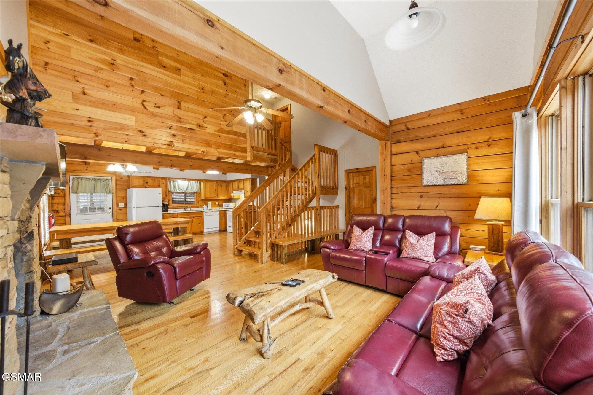 Log-cabin living room with burgundy leather sofas, stone fireplace, and open staircase to a loft.