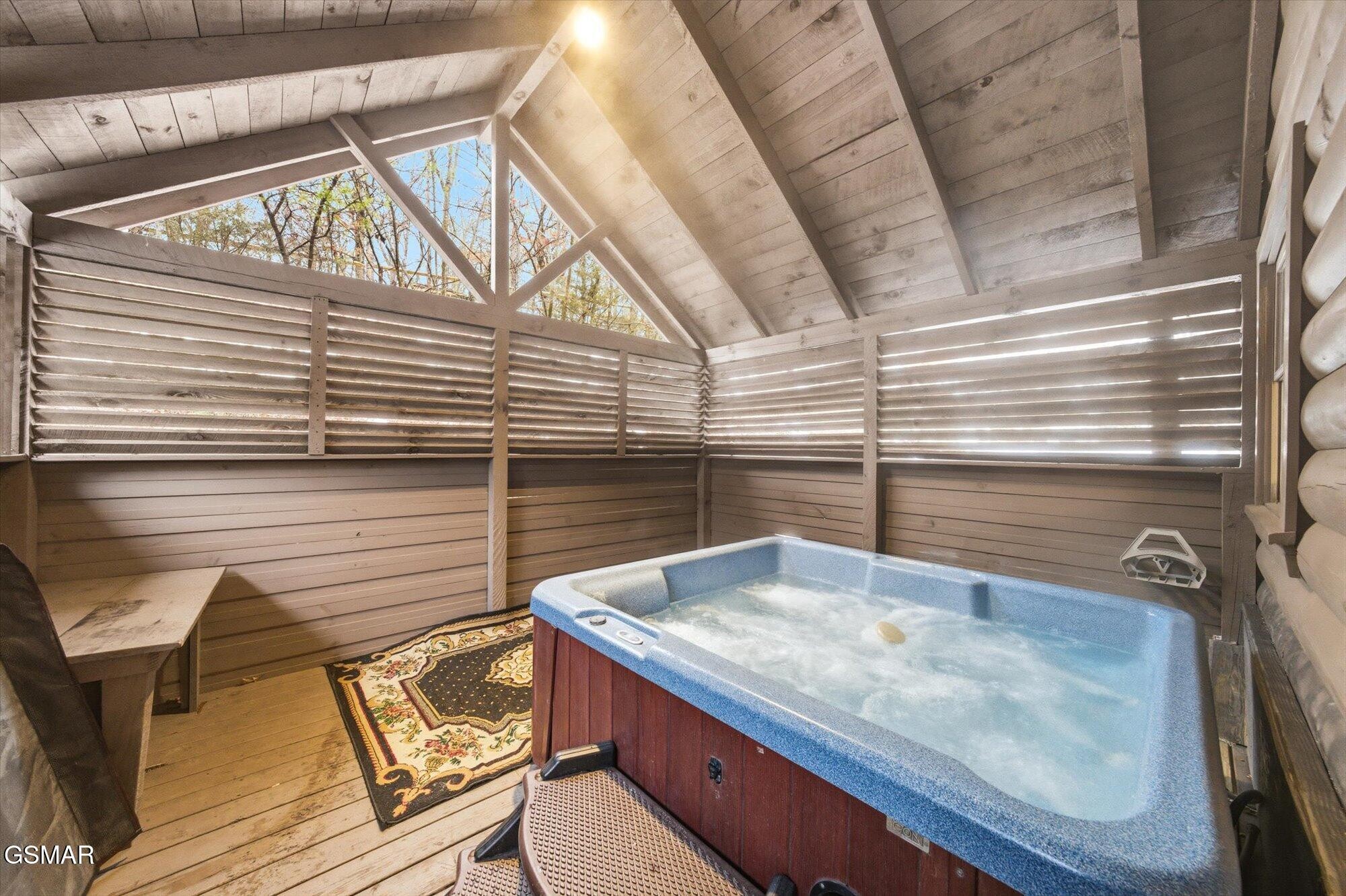 Covered wooden deck with a large hot tub, privacy fencing, and a patterned rug.