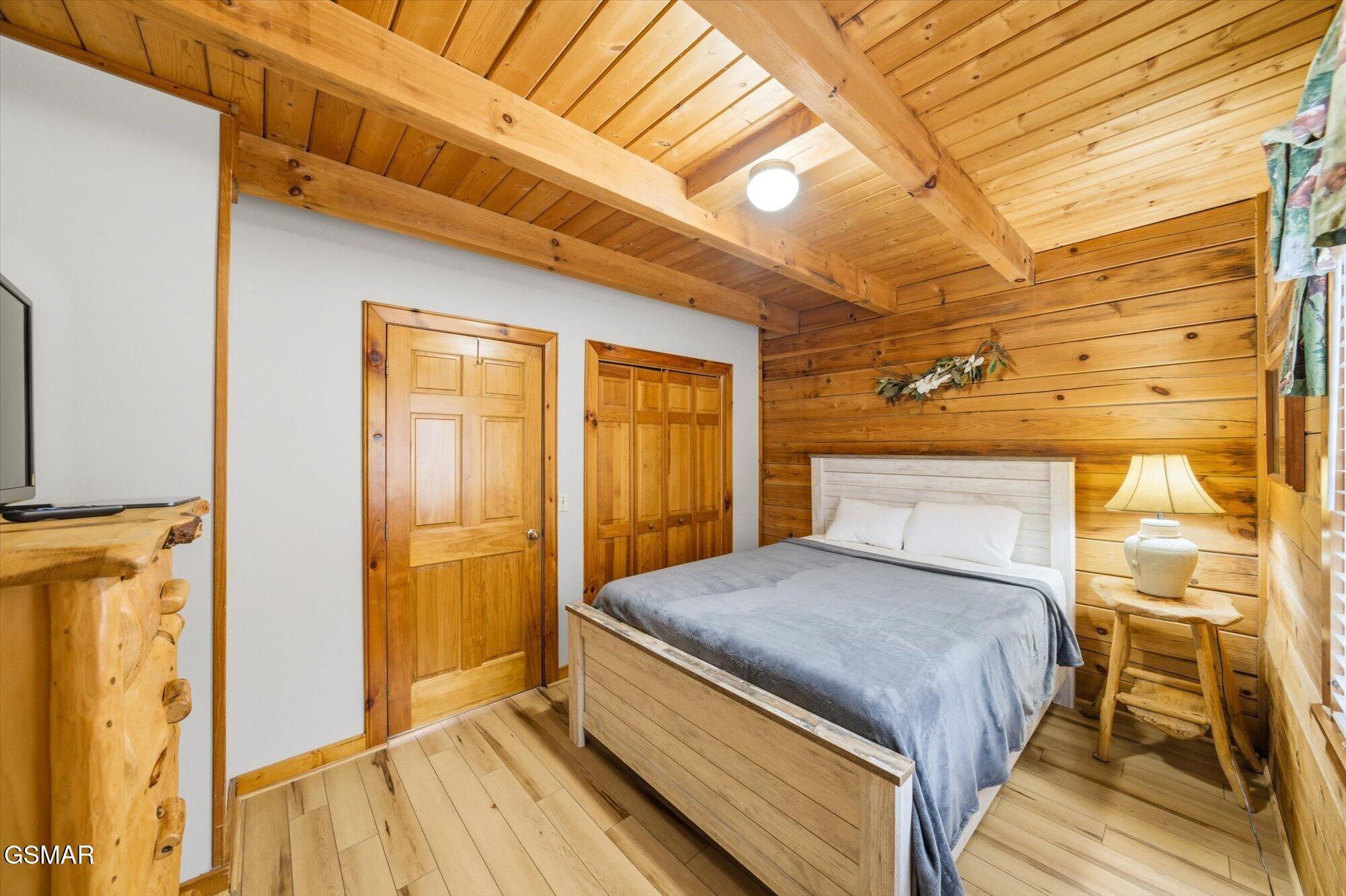 Bedroom with a gray-covered bed, pine walls, and exposed ceiling beams.