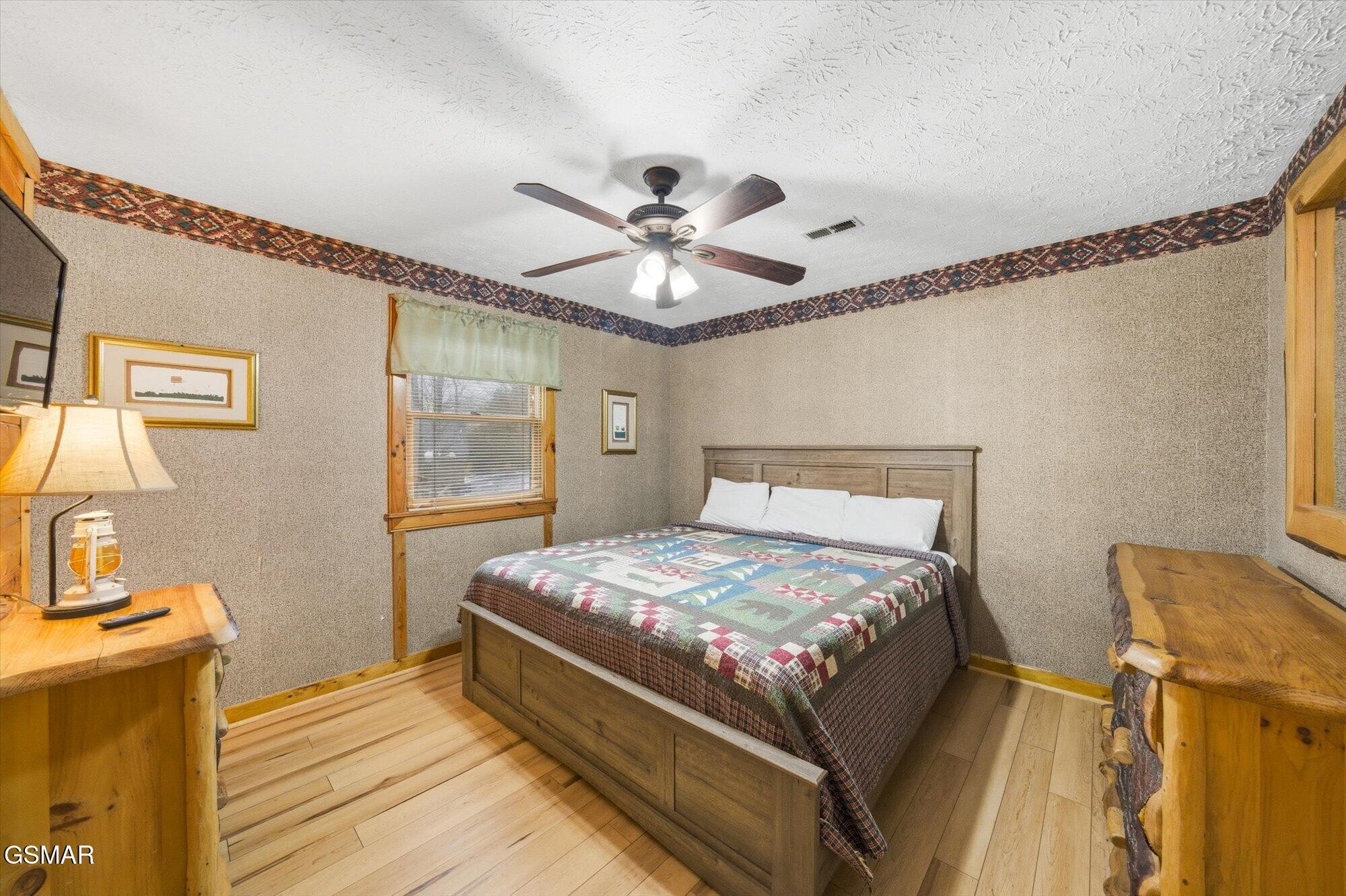 Furnished bedroom with a wooden bed, patchwork quilt, ceiling fan, and rustic wood furniture.