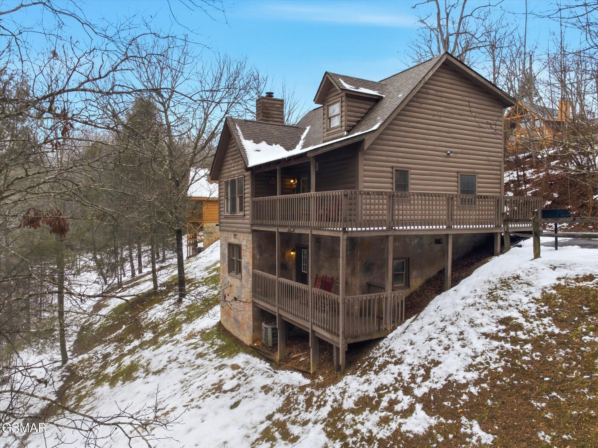 Log cabin with wraparound decks on a snowy, wooded hillside.