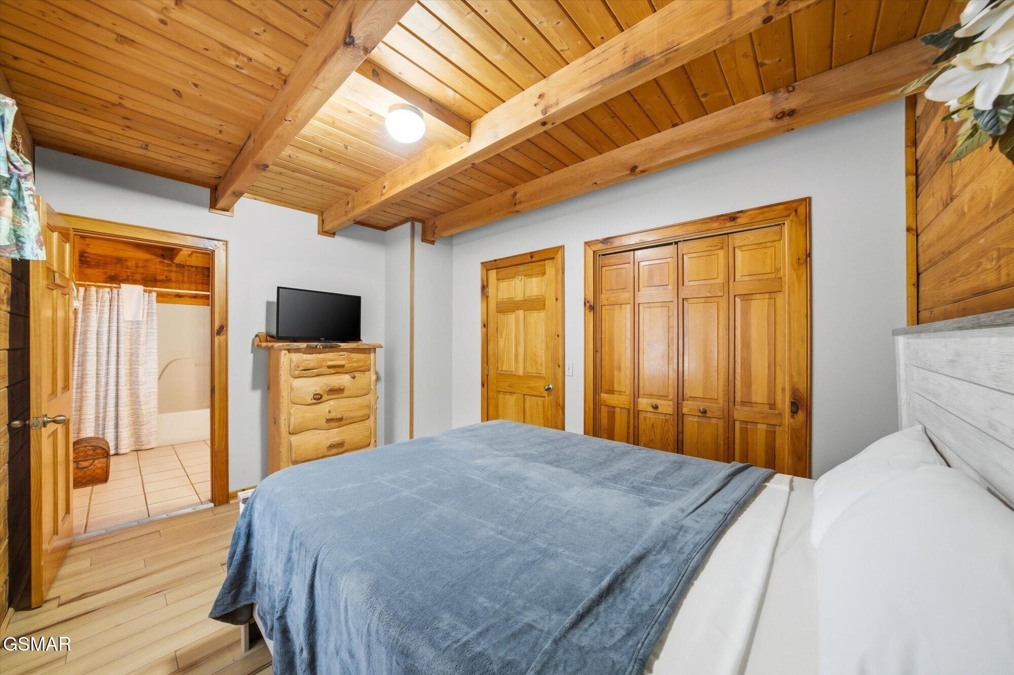 Bedroom with a blue-covered bed beneath a vaulted wood ceiling with exposed beams.