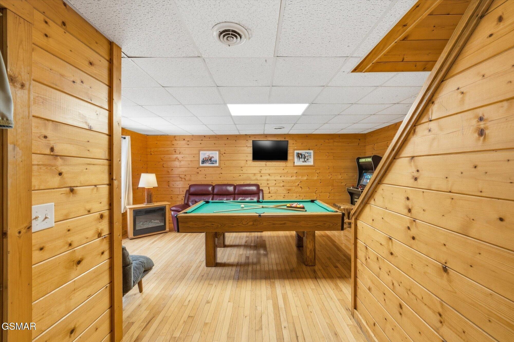 Wood-paneled game room with a pool table, leather sofa, and arcade machine.