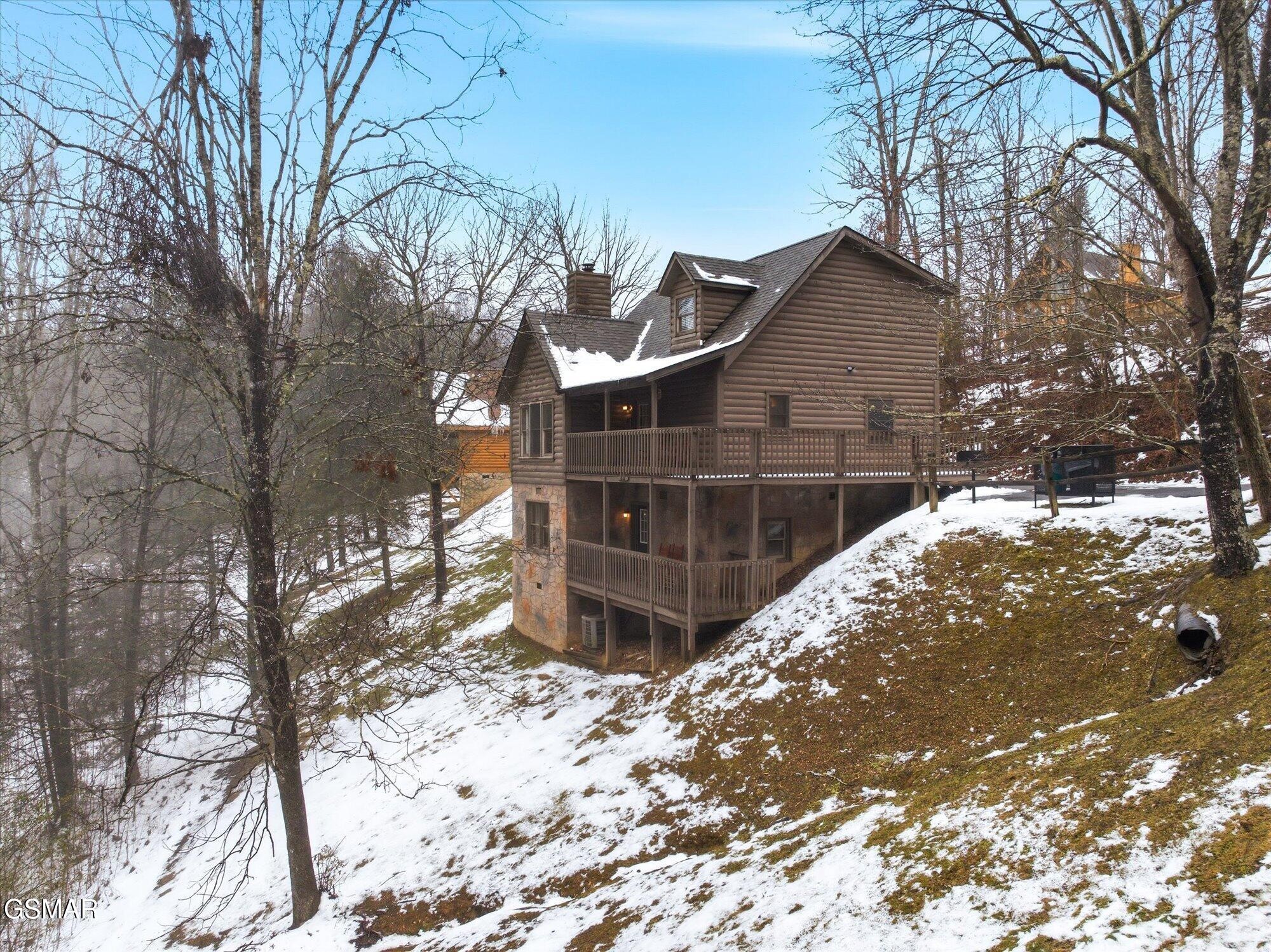 Multi-level log cabin with wraparound decks on a snowy, wooded hillside.