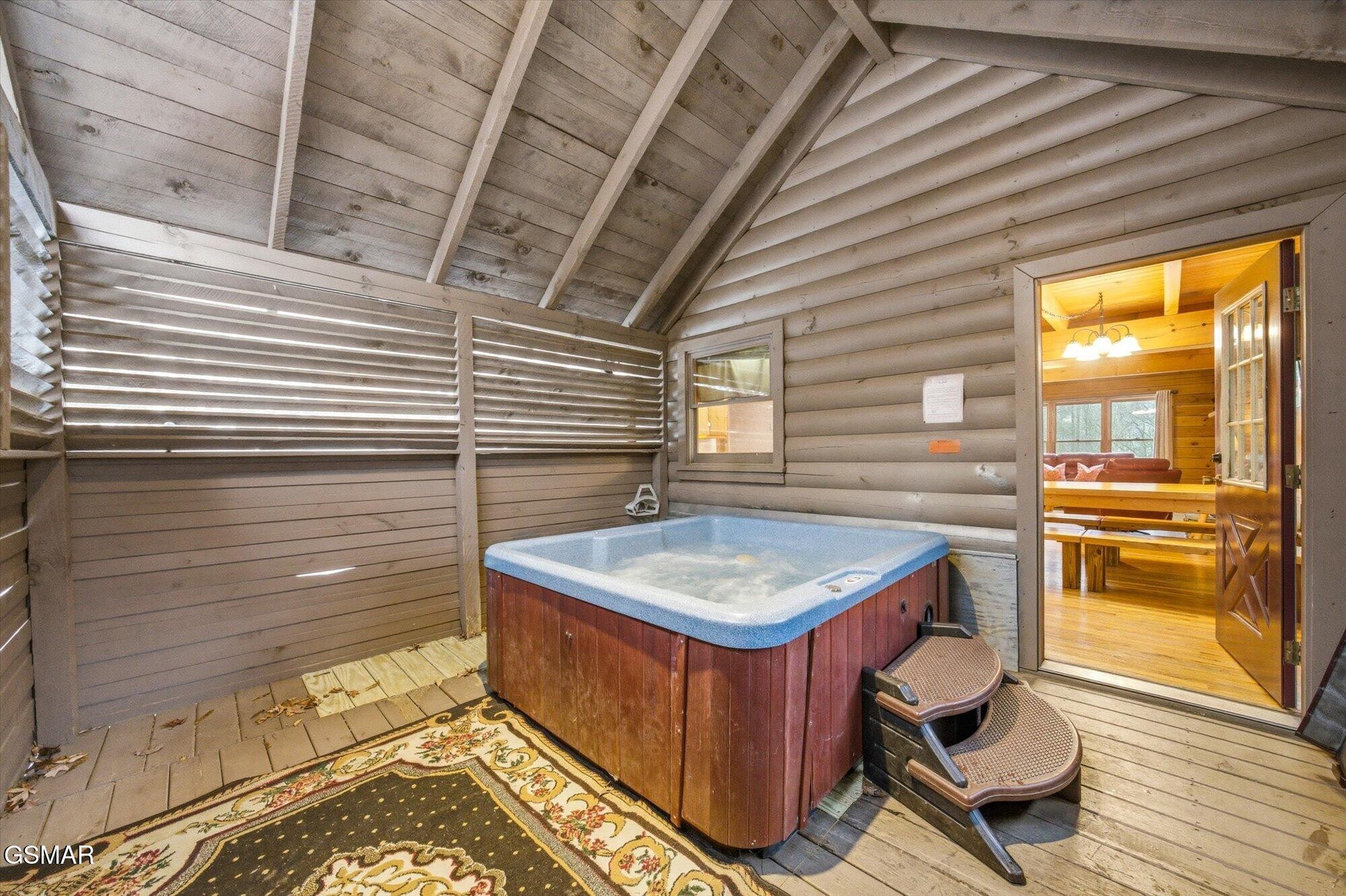 Hot tub on a covered cabin porch beside an open door to a warmly lit dining area.
