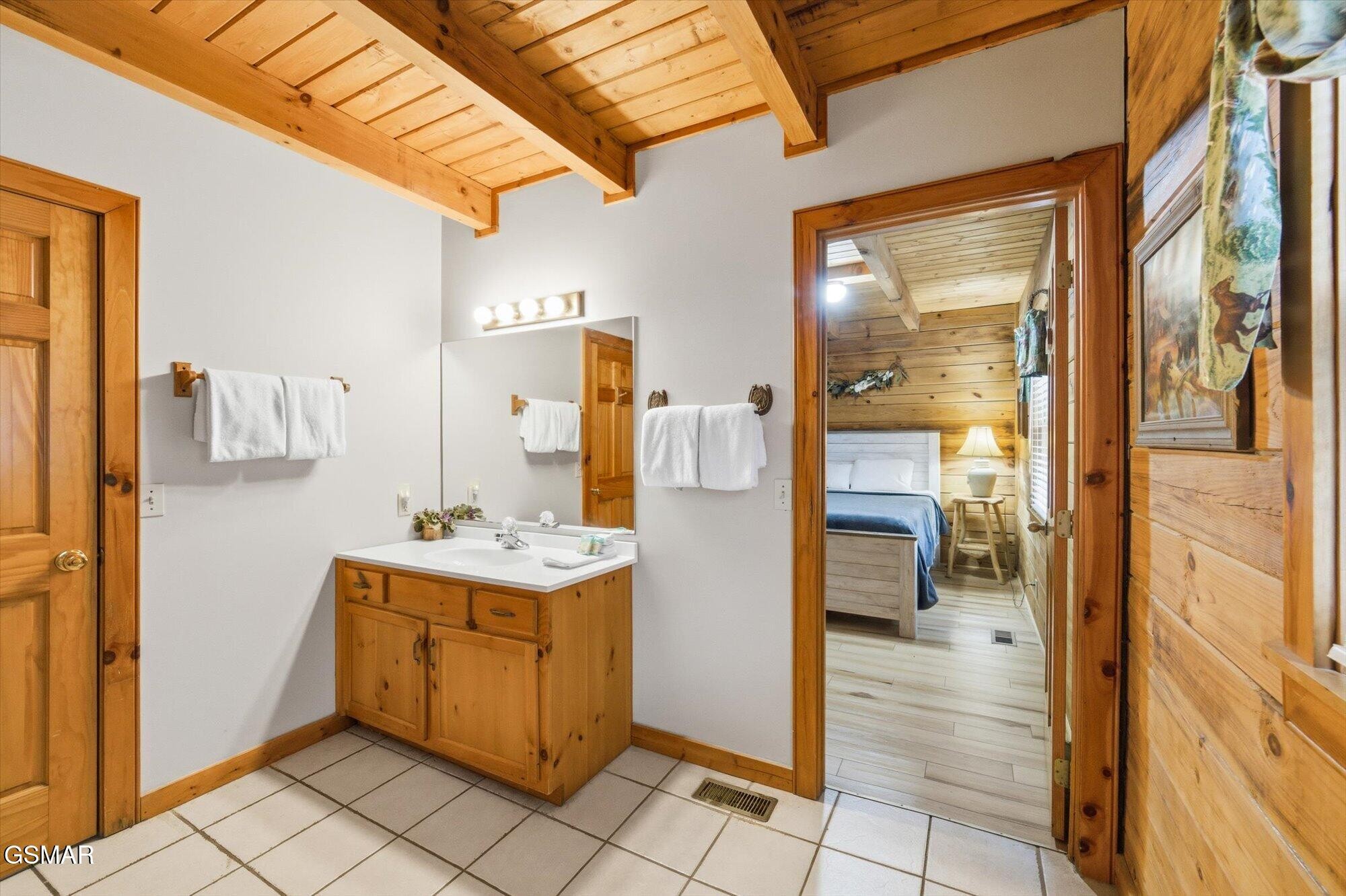 Cabin bathroom with a wooden vanity and an open doorway to a bedroom.