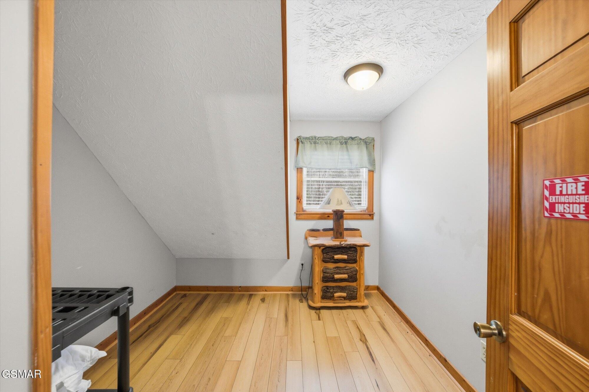 Small upstairs room with a sloped ceiling, wood flooring, a window, and rustic wooden dresser.
