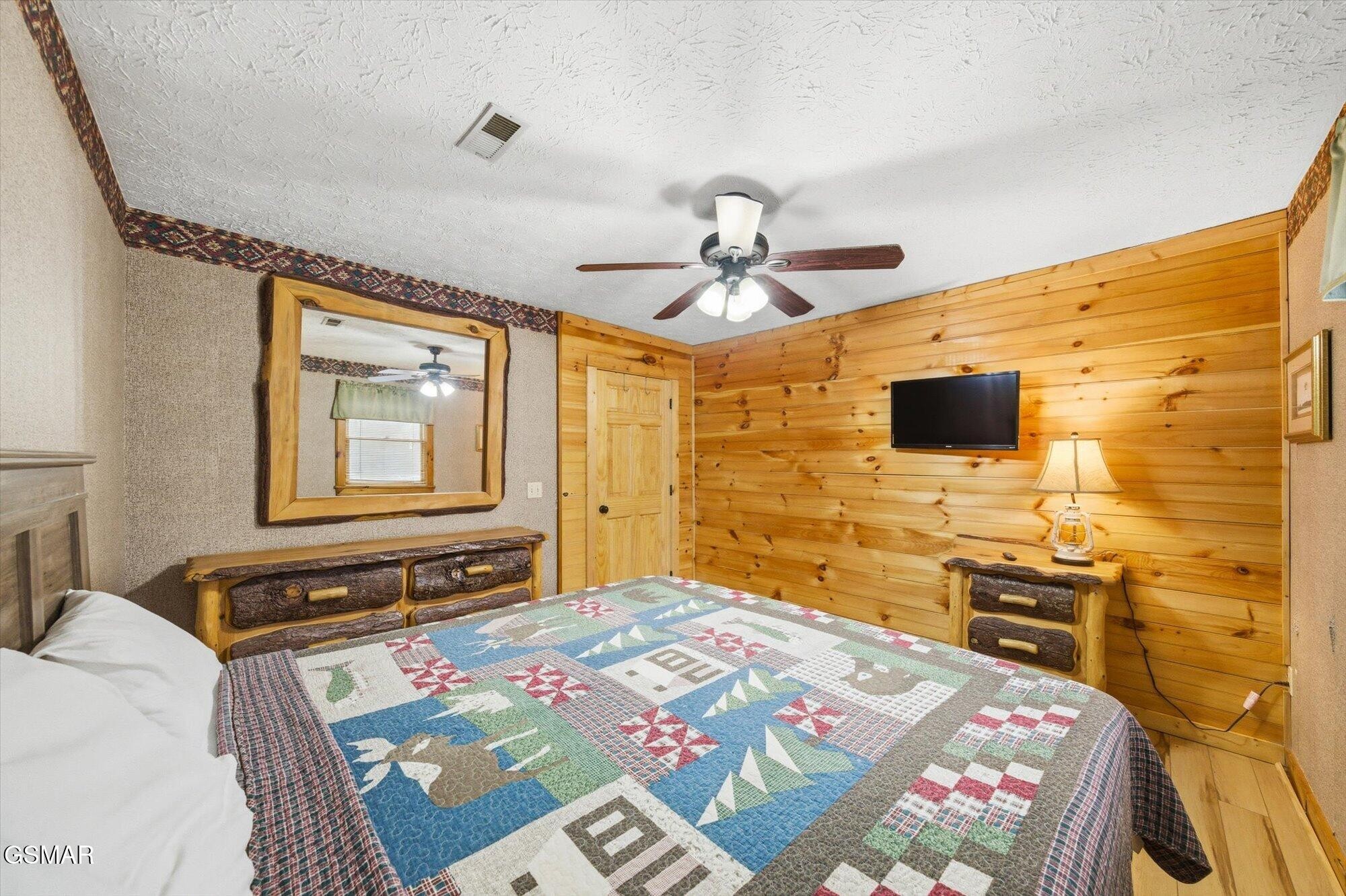 Bedroom with warm wood-paneled walls, rustic dressers, and a colorful patchwork quilt.