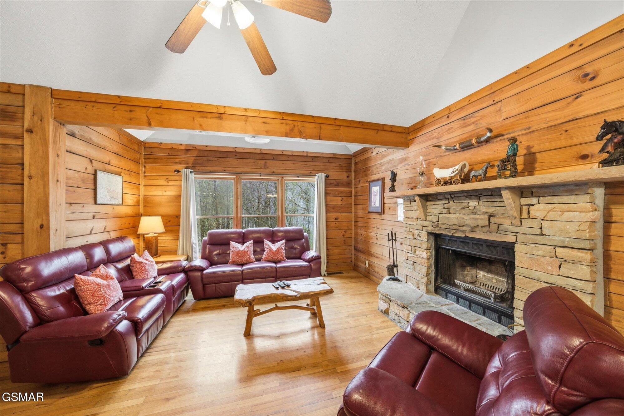 Wood-paneled living room with burgundy leather sofas and a large stone fireplace.