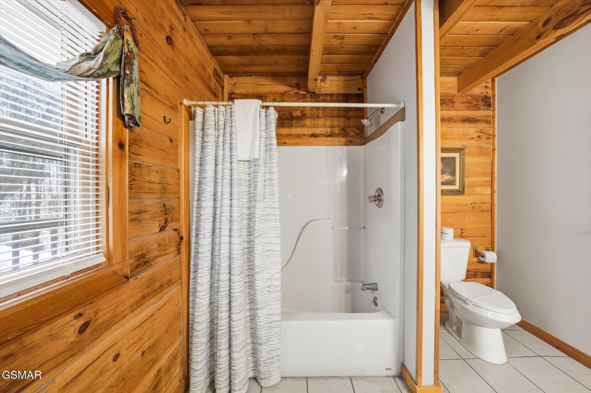 Cabin bathroom with knotty-pine walls, a white tub and shower, and a toilet in a separate nook.