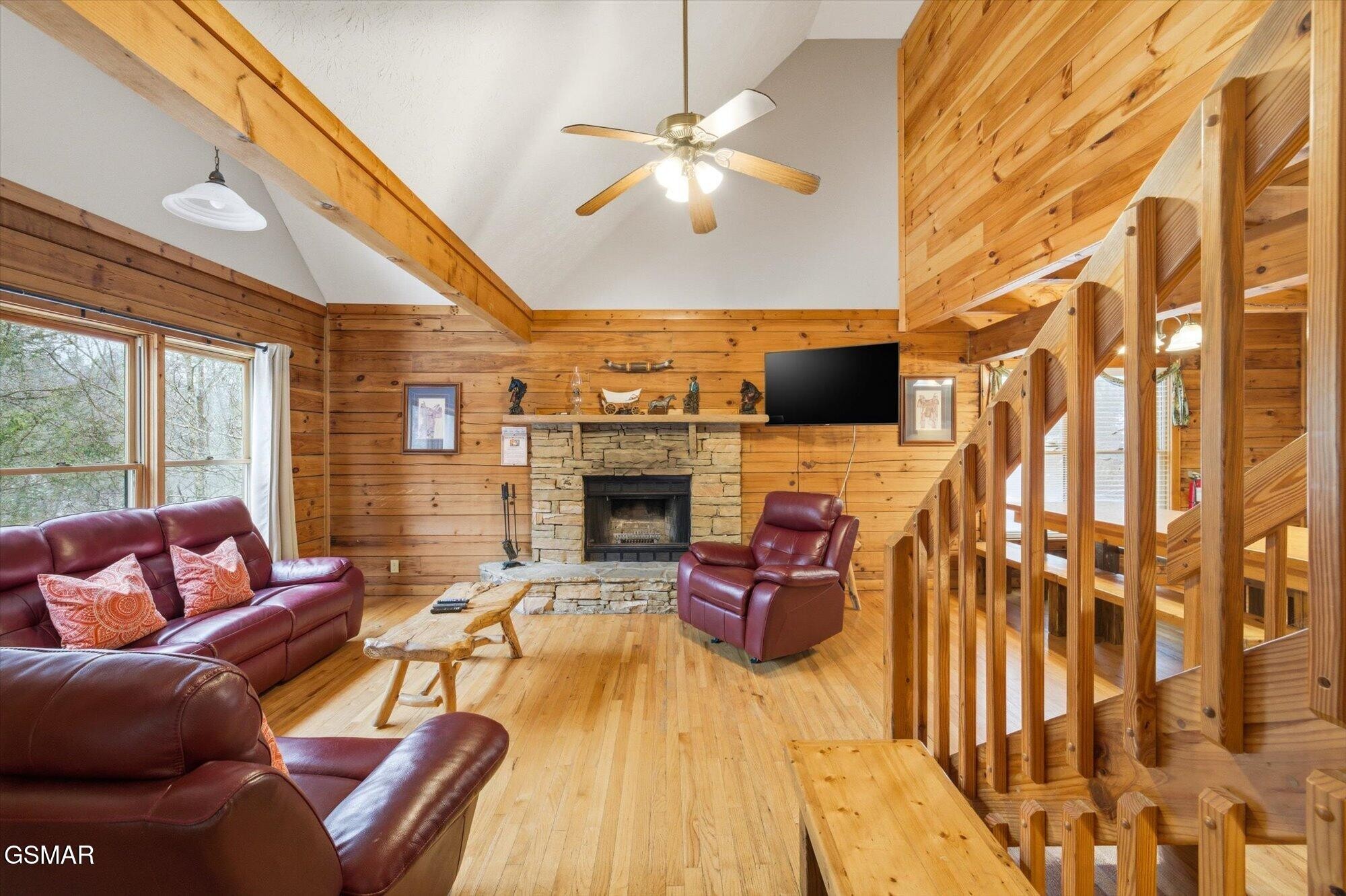 Cabin living room with a stone fireplace, vaulted wood ceiling, and burgundy leather seating.