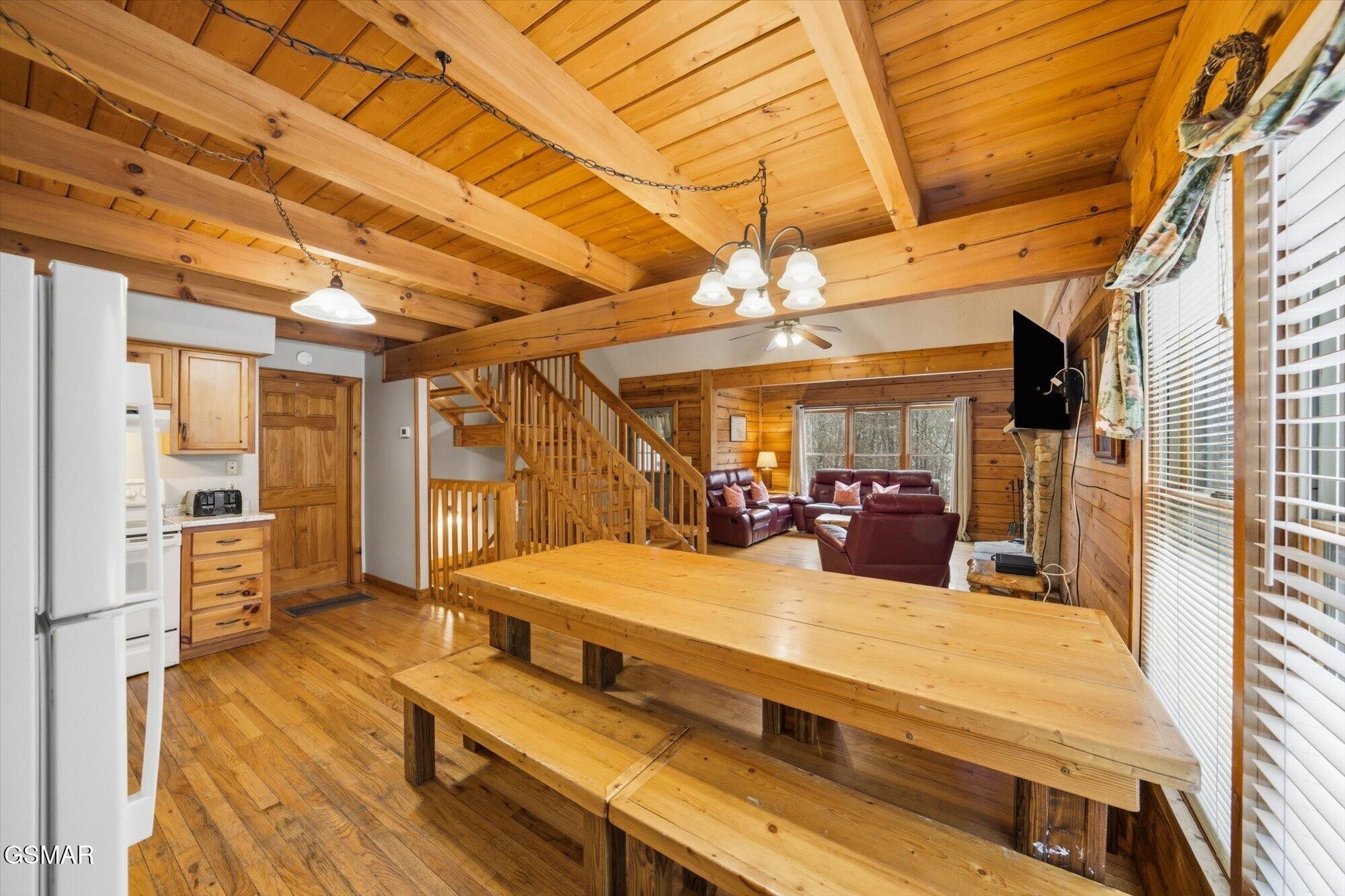 Cabin dining and living area with a large wooden table, exposed beams, staircase, and leather seating.