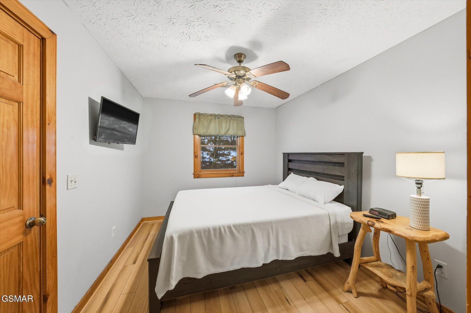Bedroom with a dark wood bed, ceiling fan, wall-mounted television, and wood floors.