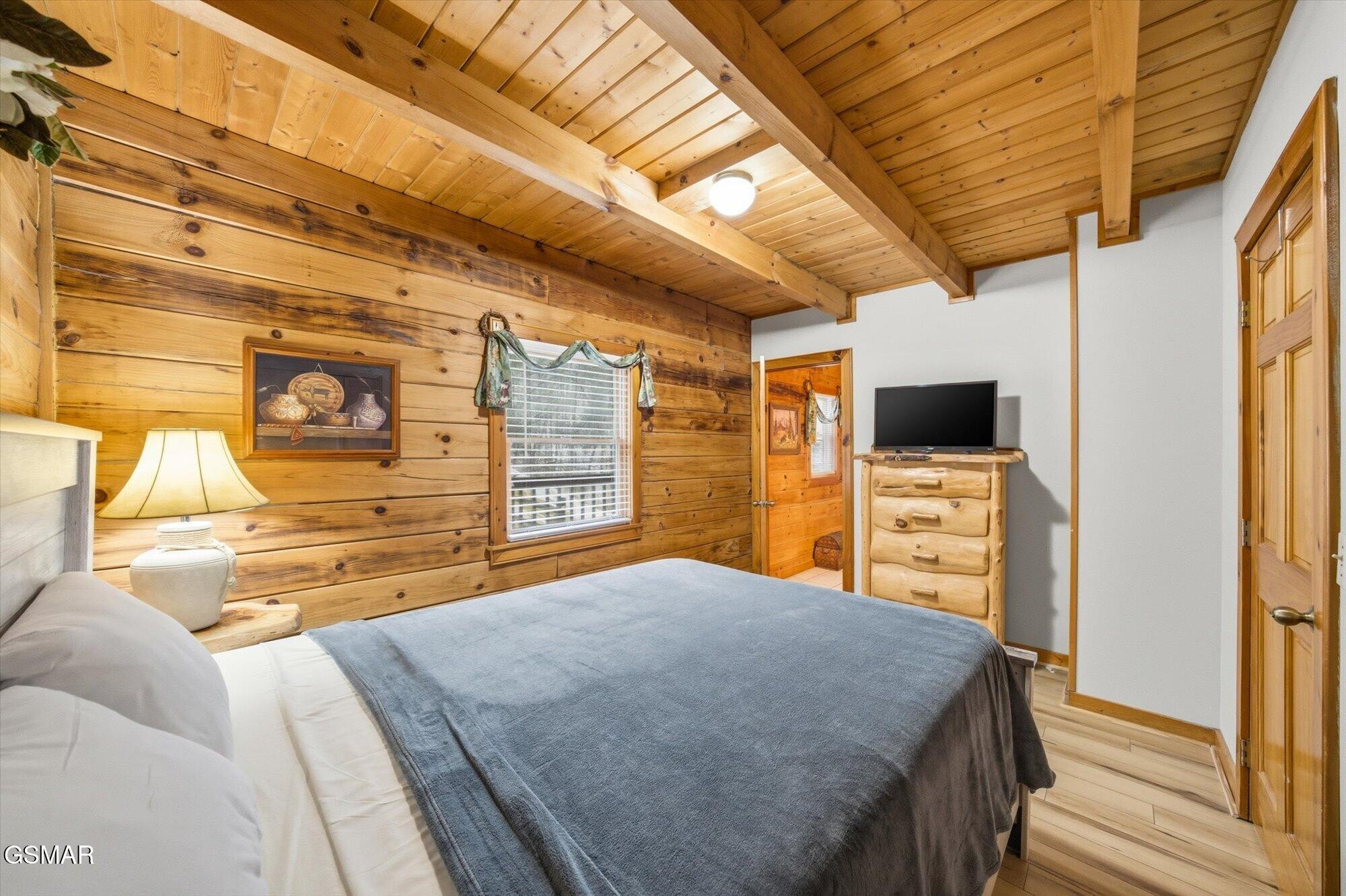 Rustic bedroom with a vaulted wood ceiling, knotty-pine walls, and a bed facing a television.