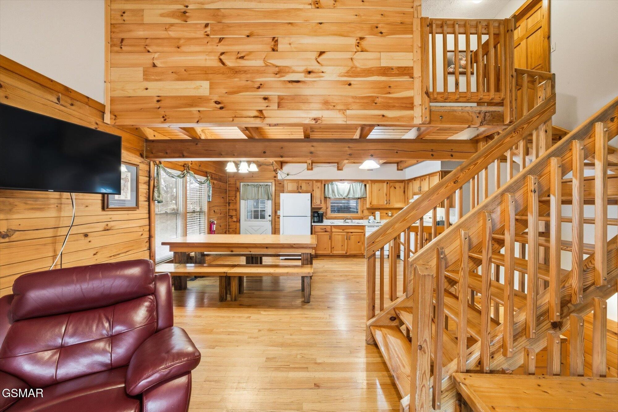 Open-plan cabin living area with a pine staircase, dining table, kitchen, and burgundy leather recliner.