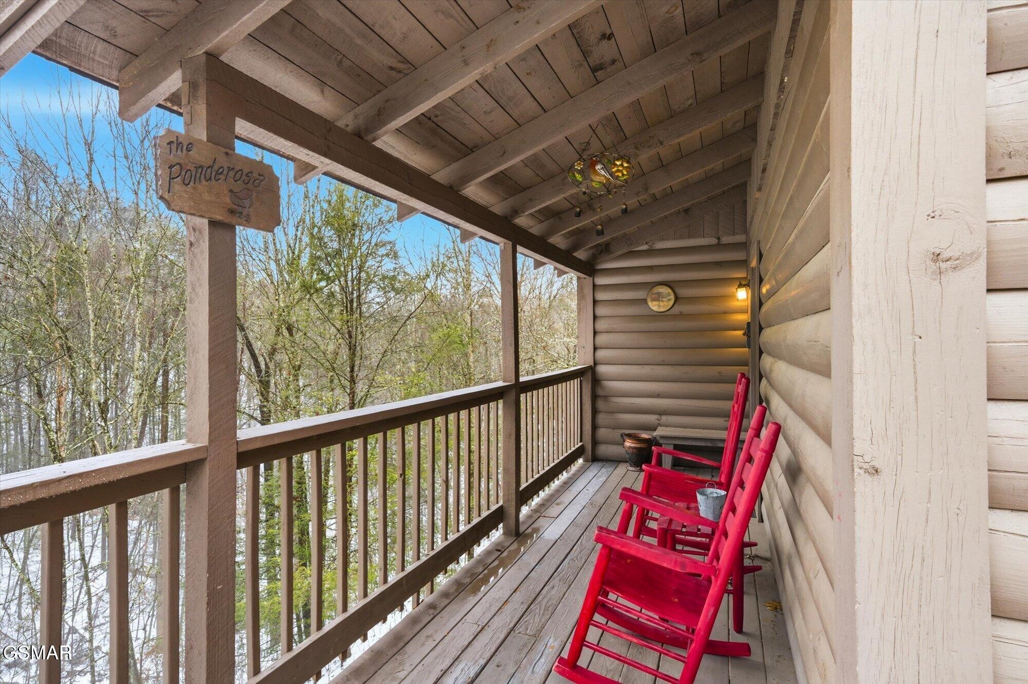 Covered wooden porch with bright red chairs overlooking leafing trees.
