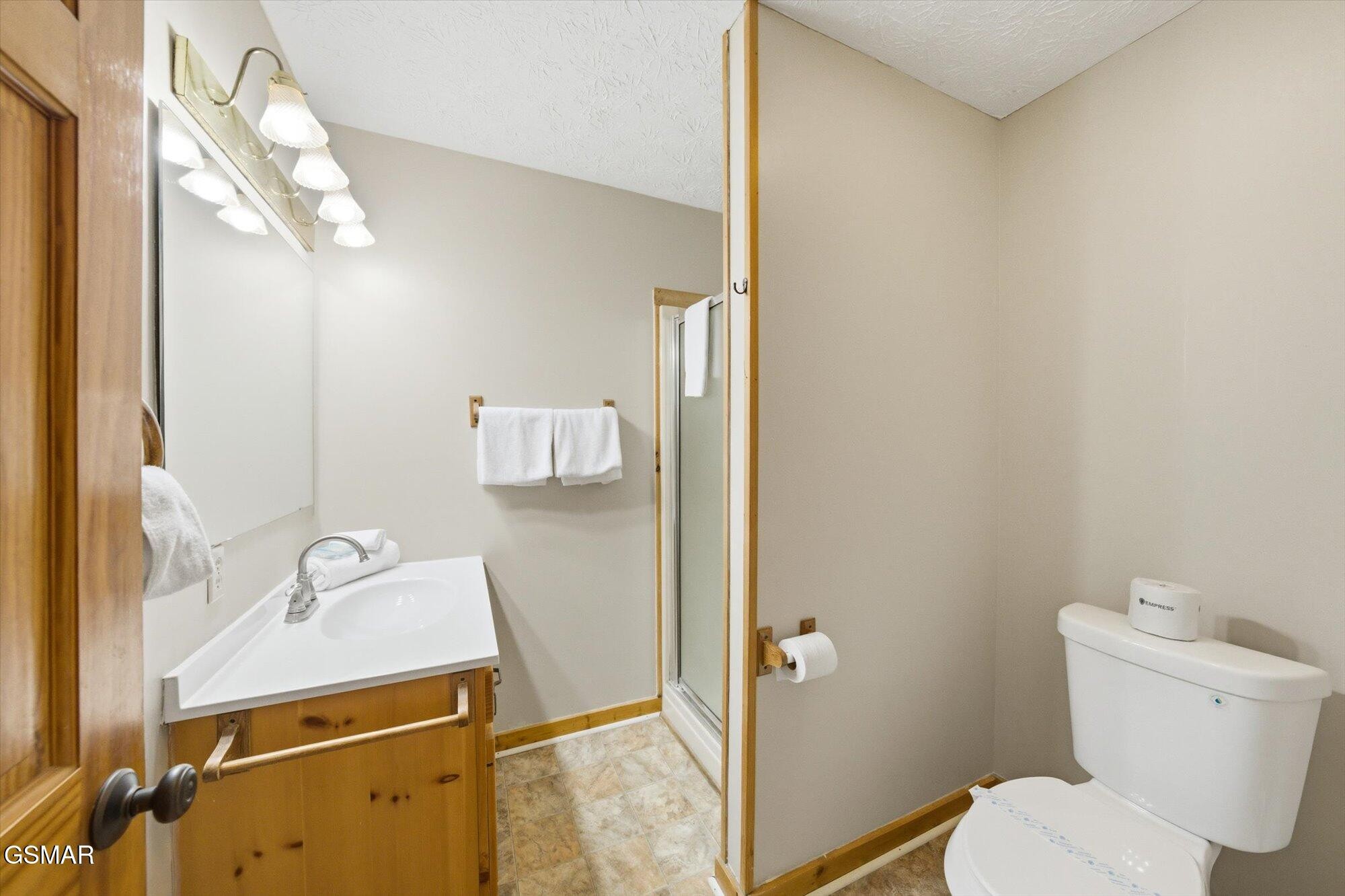 Bathroom with a wood vanity, large mirror, glass shower, white towels, and toilet.