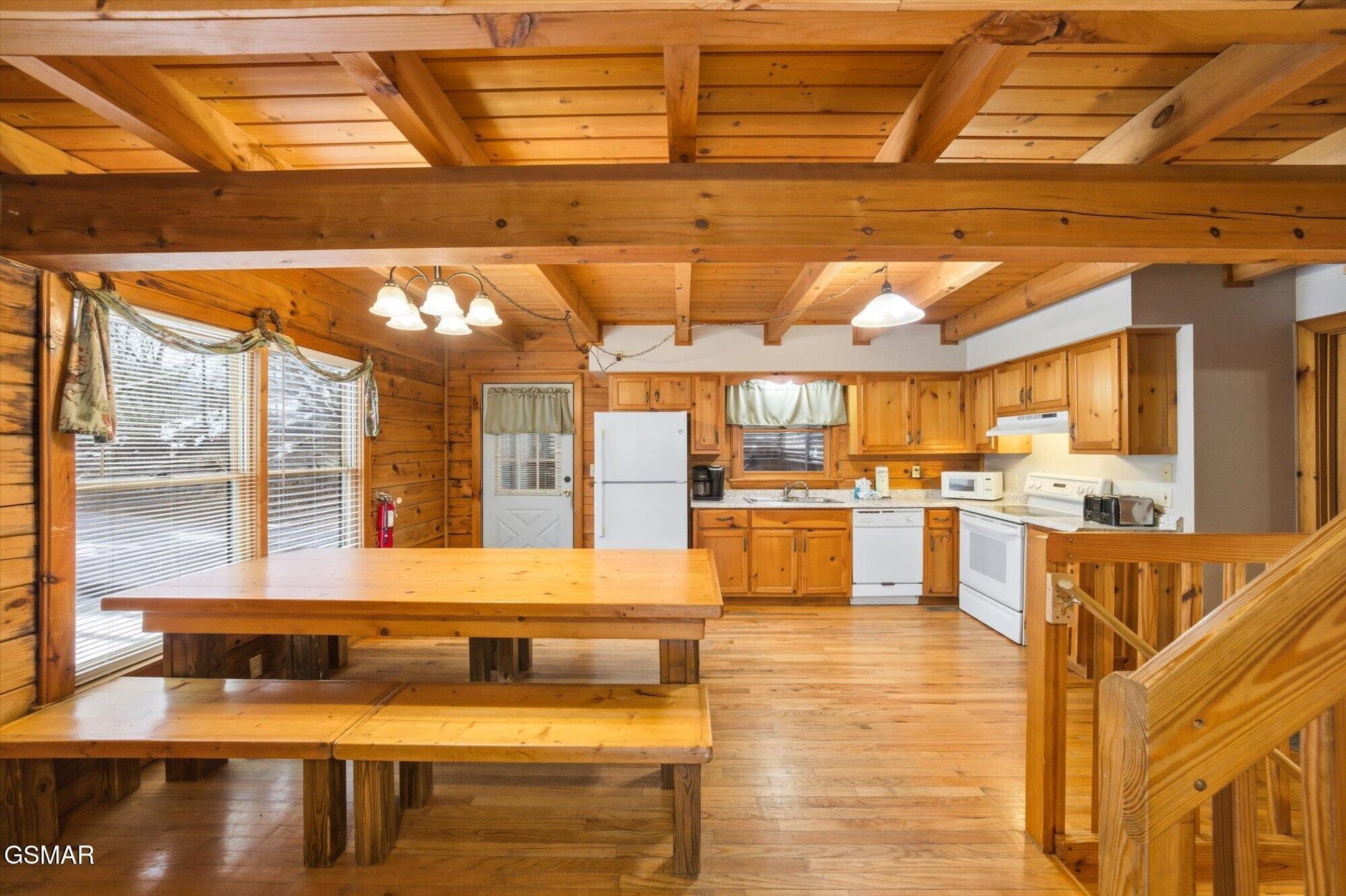 Wood-paneled kitchen with exposed beams, white appliances, and a large wooden dining table.