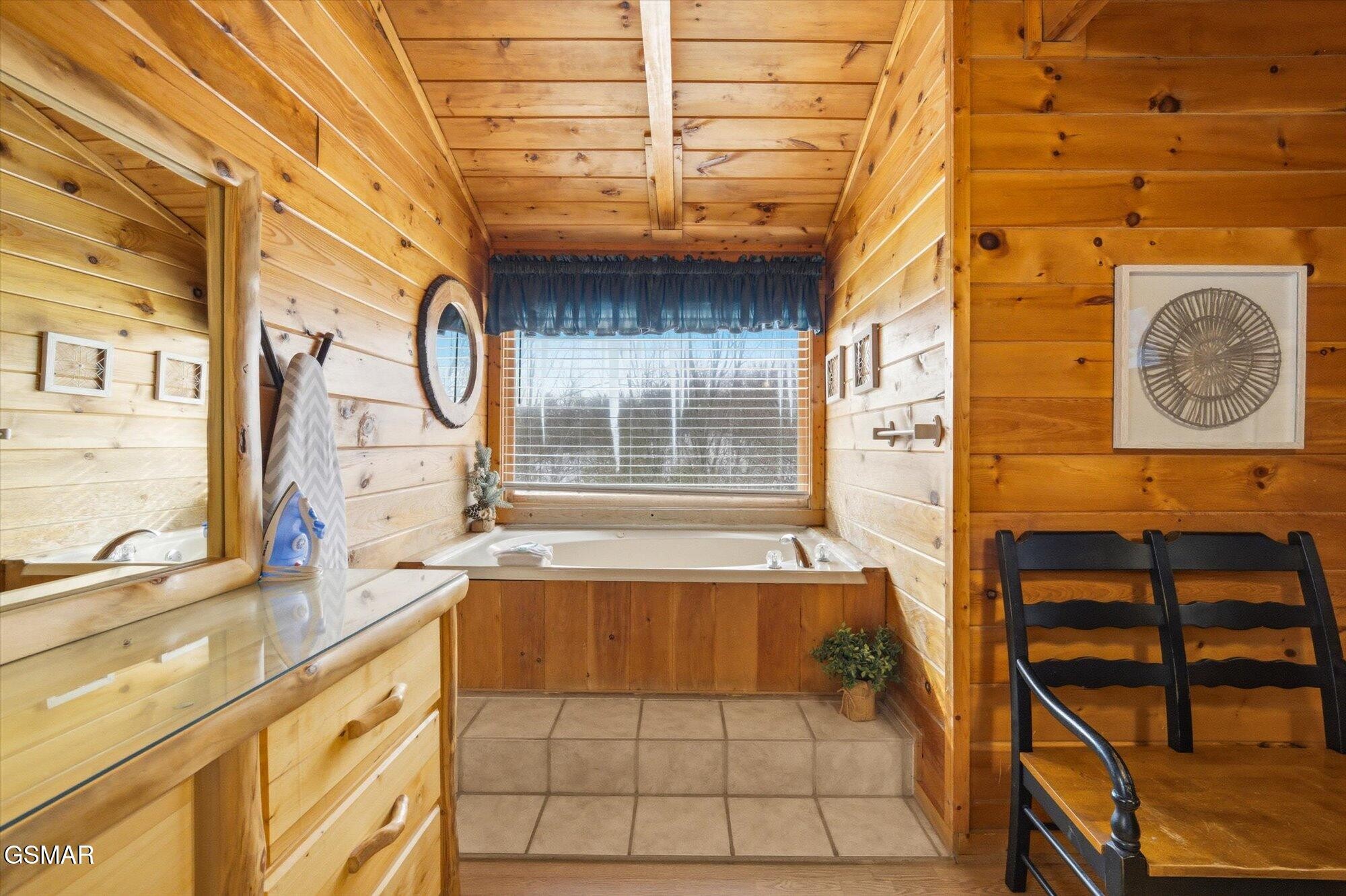 Wood-paneled bathroom with a built-in tub beneath a window and a wooden bench beside it.
