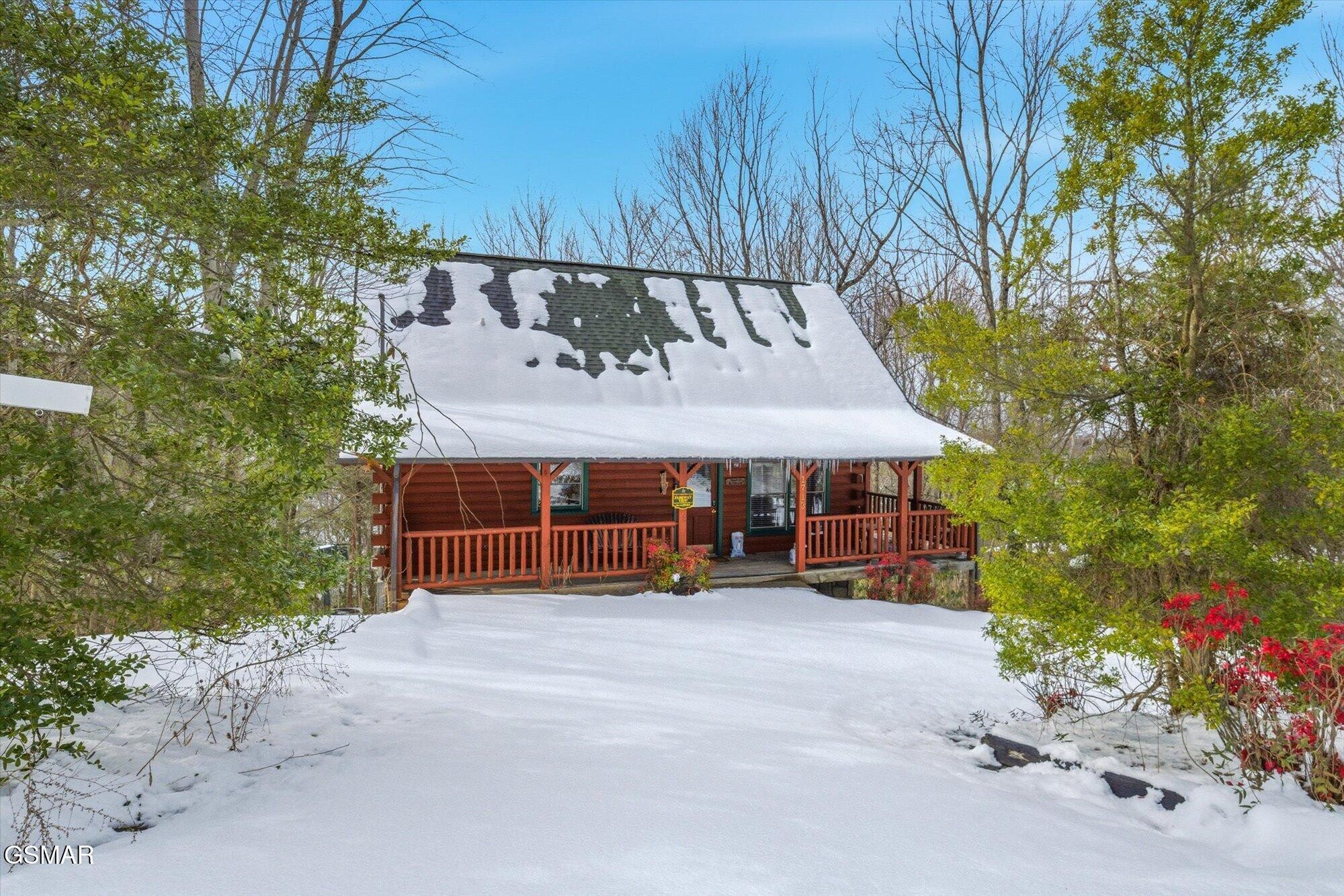 Log cabin with a covered porch, surrounded by trees and a snow-covered yard.