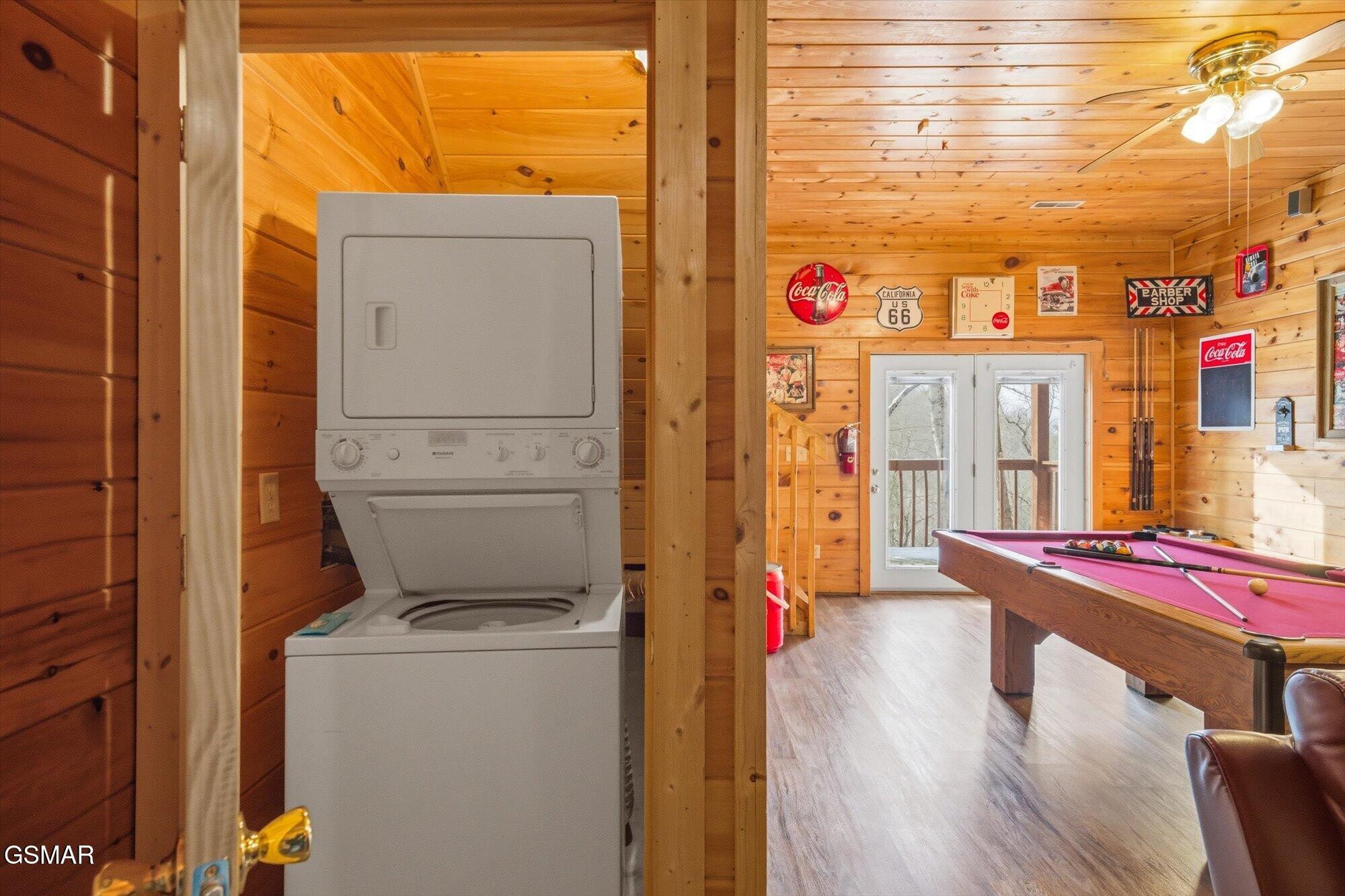 Wood-paneled cabin game room with a pink pool table and stacked washer and dryer.