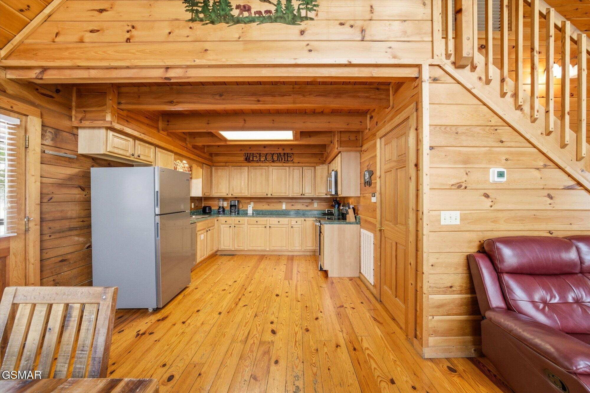 Log-cabin kitchen with exposed beams, light wood cabinets, and a stainless-steel refrigerator.