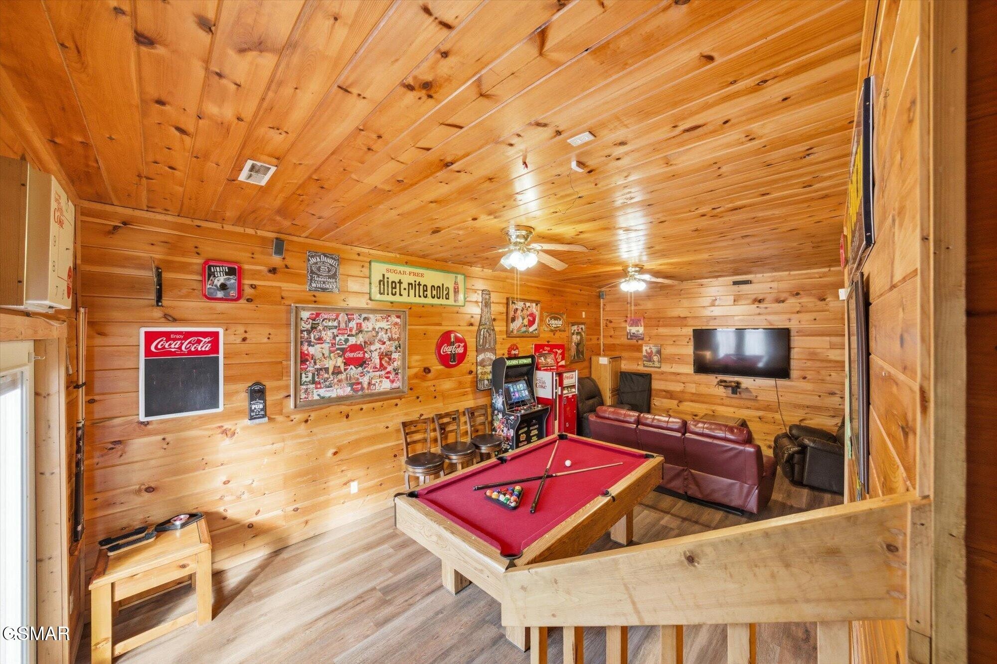 Wood-paneled game room with a red pool table, arcade game, and leather seating.