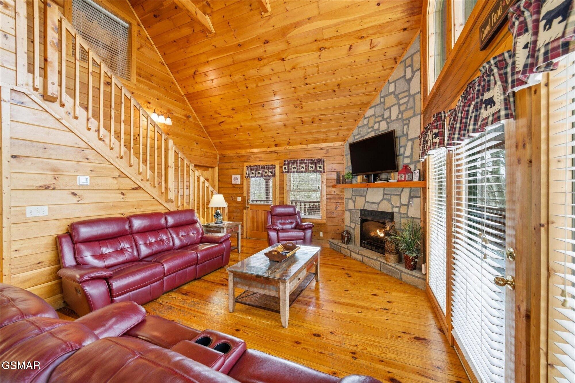 Cabin living room with red leather seating, a wood staircase, and a stone fireplace.