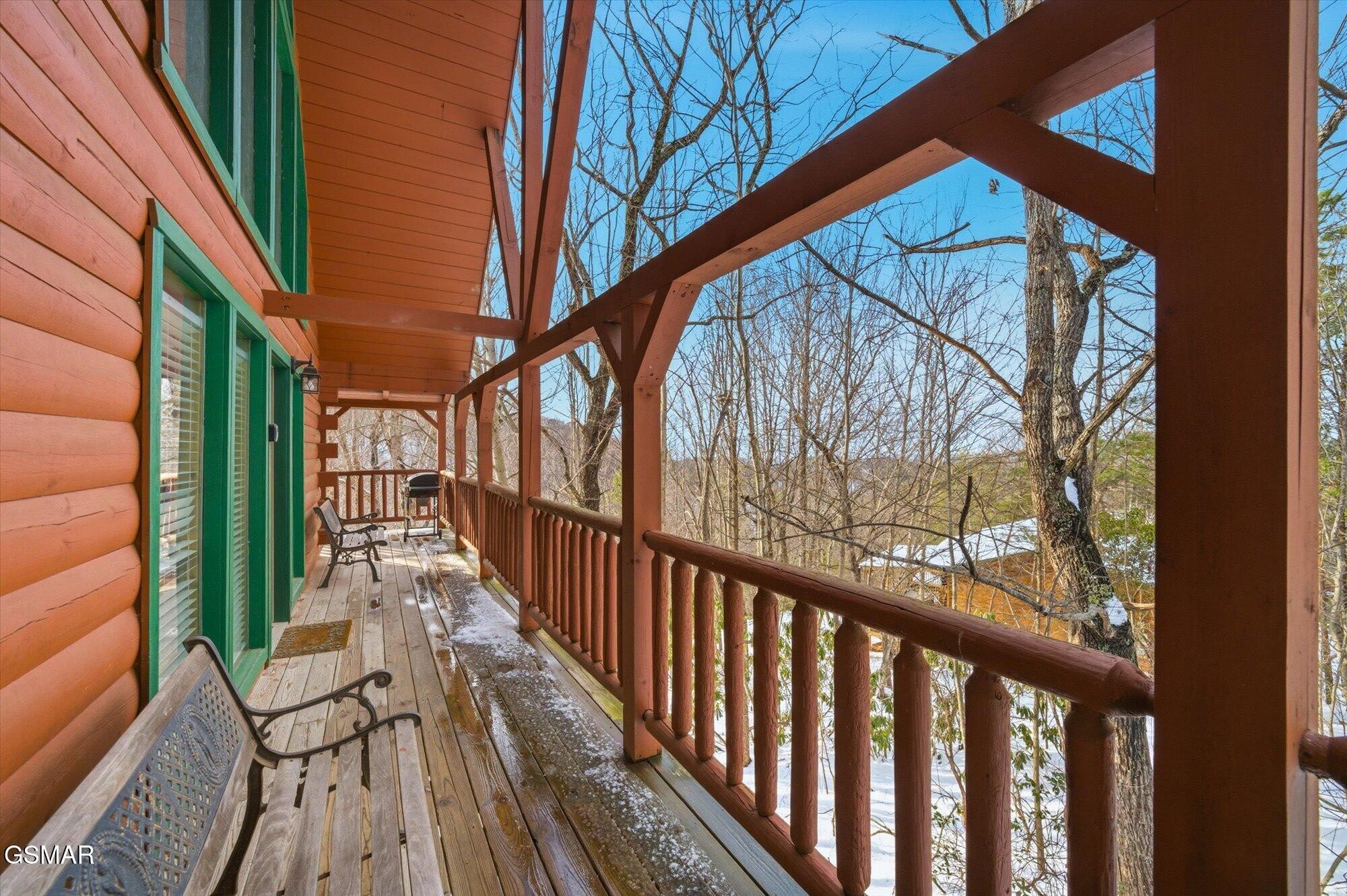 Cabin porch with wooden railings, chairs, and a wooded winter view.