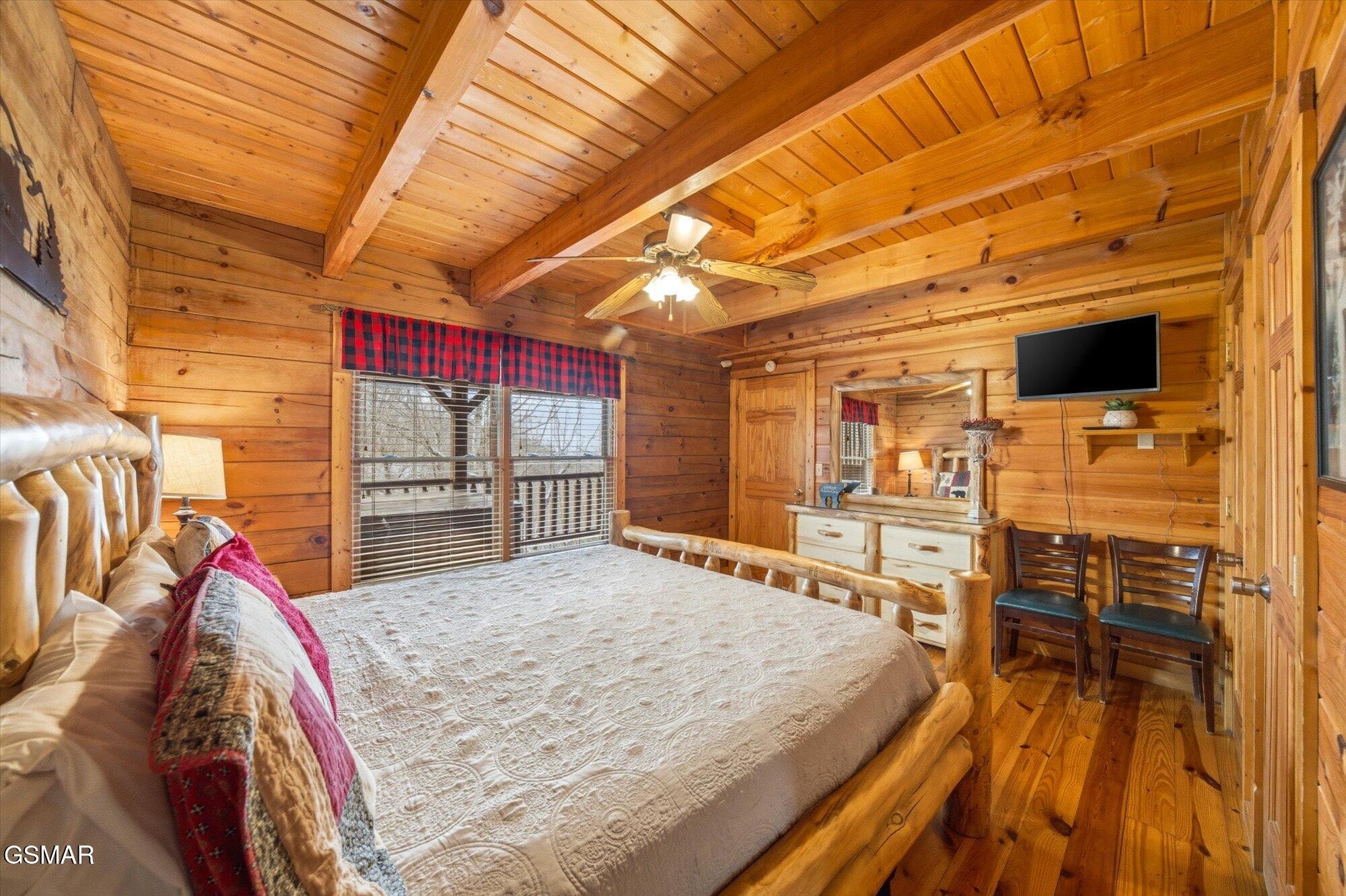 Log-cabin bedroom with a log-frame bed, exposed beams, and red plaid window valance.
