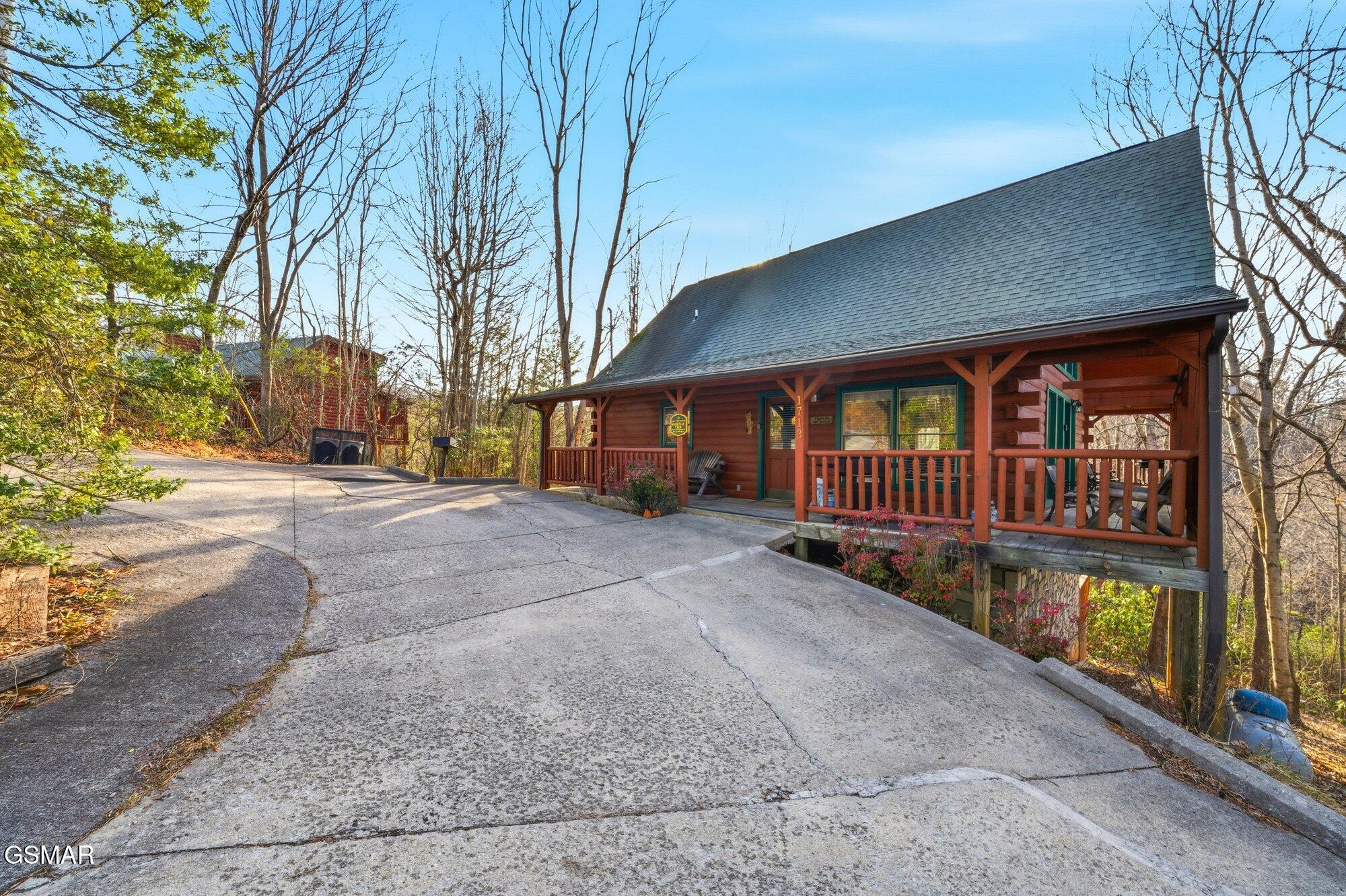 Red log cabin with a covered porch beside a sloping concrete driveway.
