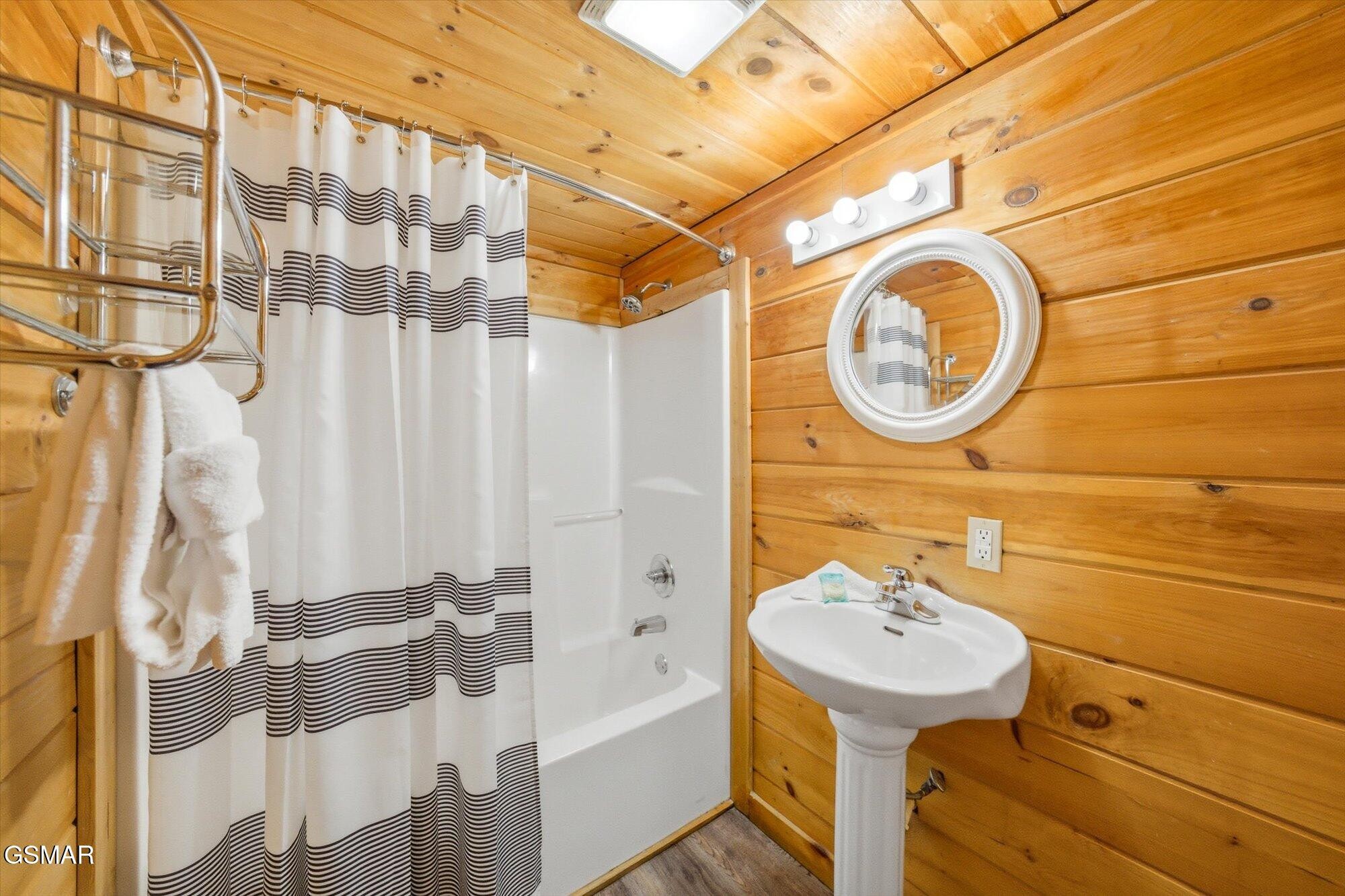 Bathroom with wood-paneled walls, a white tub behind a striped curtain, and a pedestal sink.