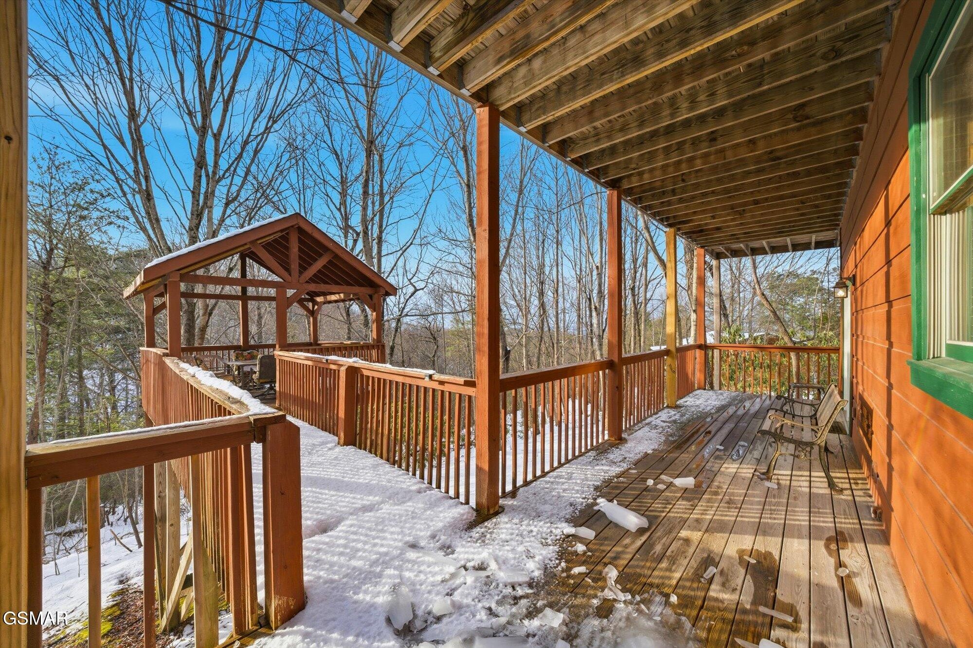 Covered wooden deck with gazebo and chairs, dusted with snow beside an orange-sided home.