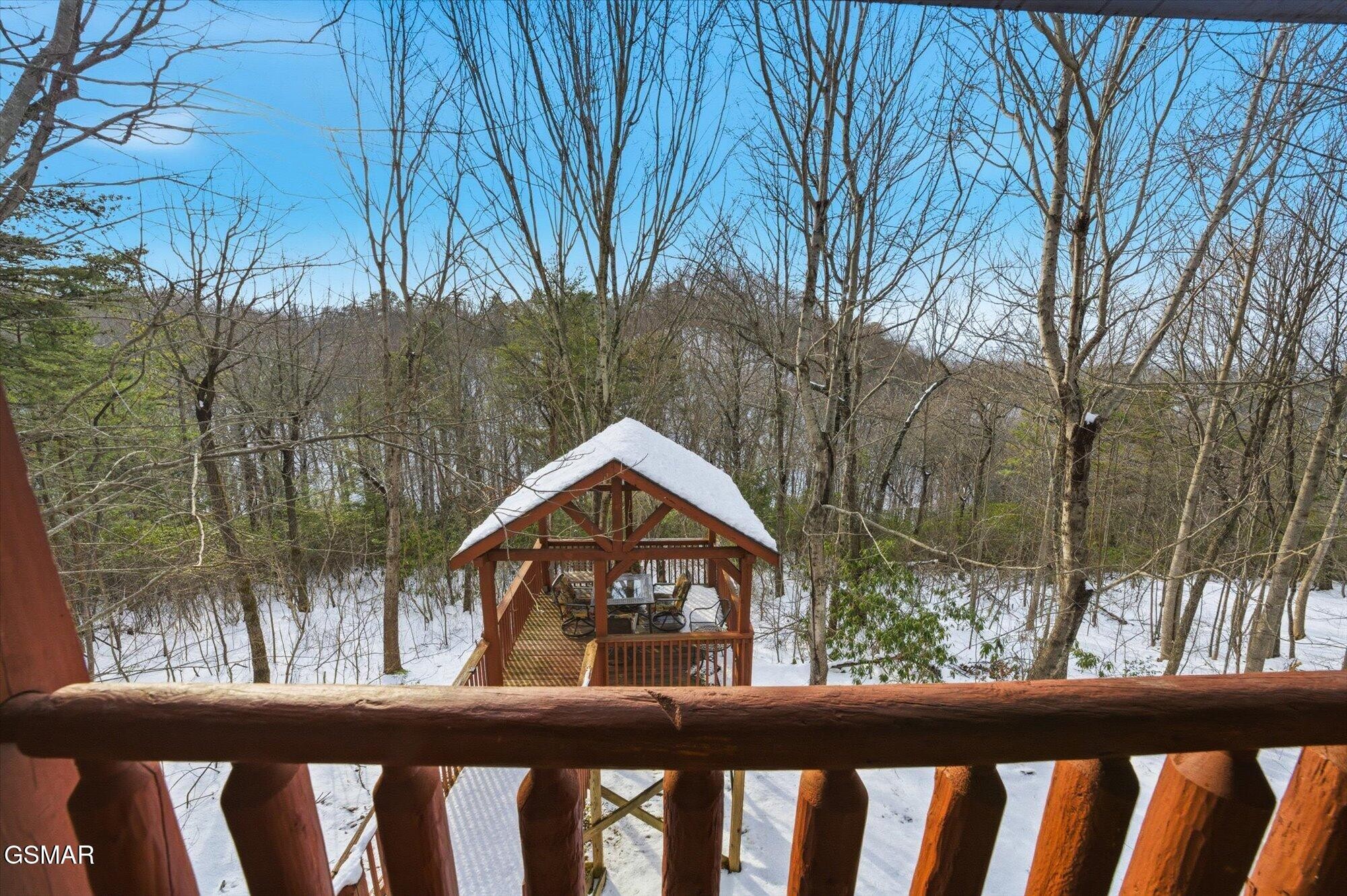 Snow-covered wooded property and covered gazebo viewed from a wooden deck.