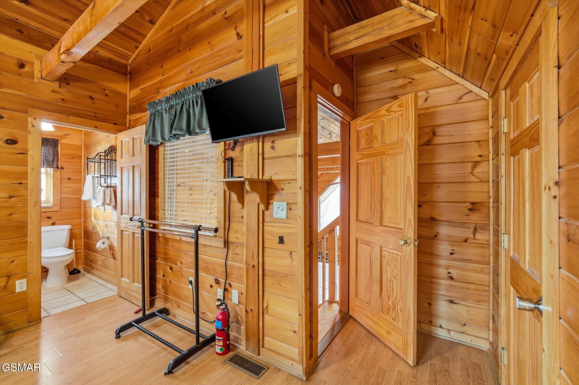 Wood-paneled cabin interior with a wall-mounted TV, exercise barre, and open bathroom doorway.