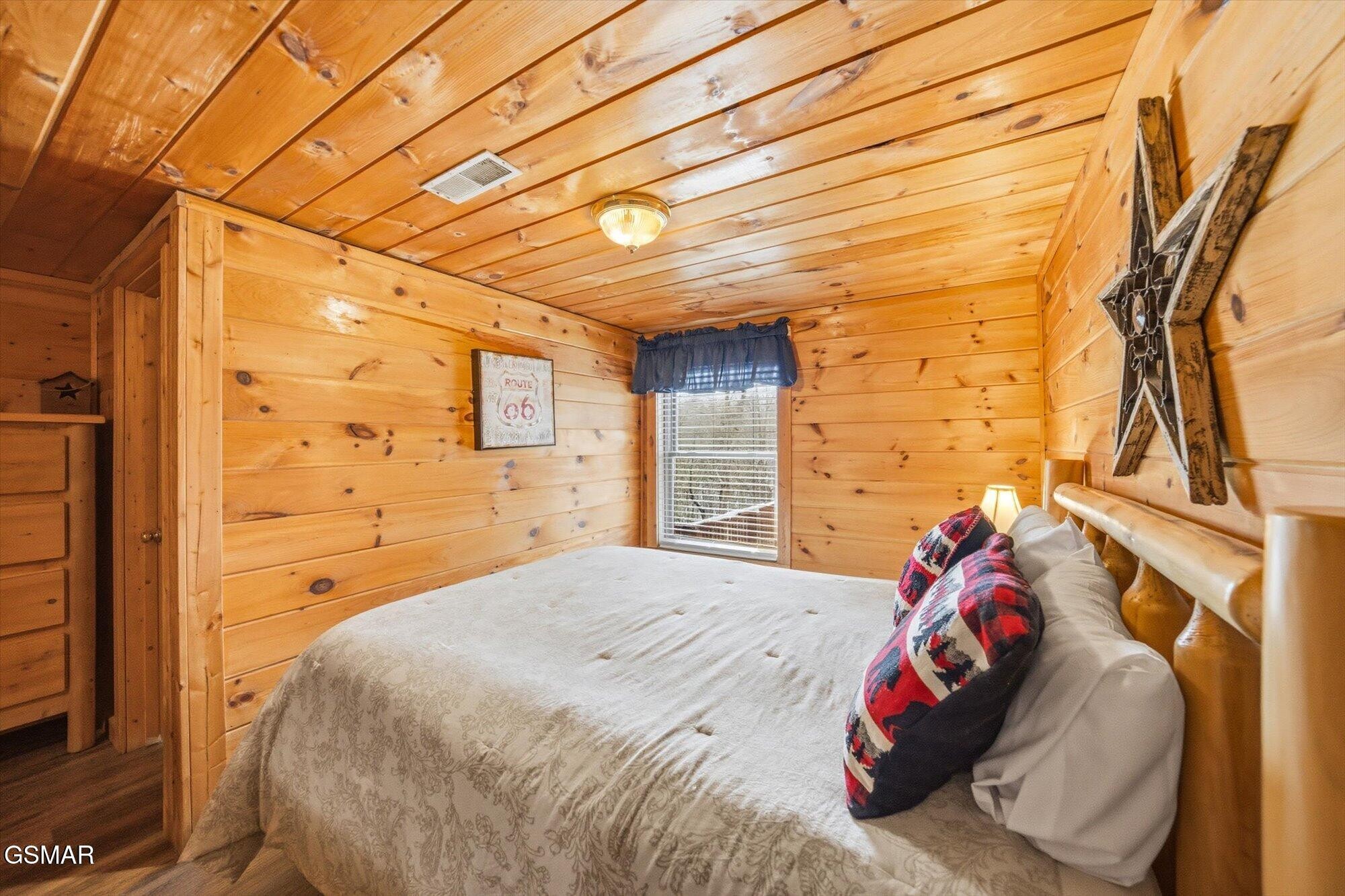 Wood-paneled bedroom with a white-covered bed, plaid pillows, and a window with blinds.