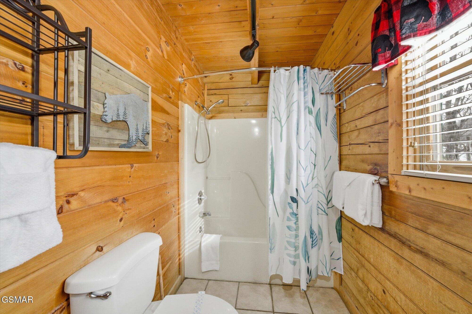 Cabin bathroom with wood-plank walls, a white shower, and a leafy-patterned curtain.