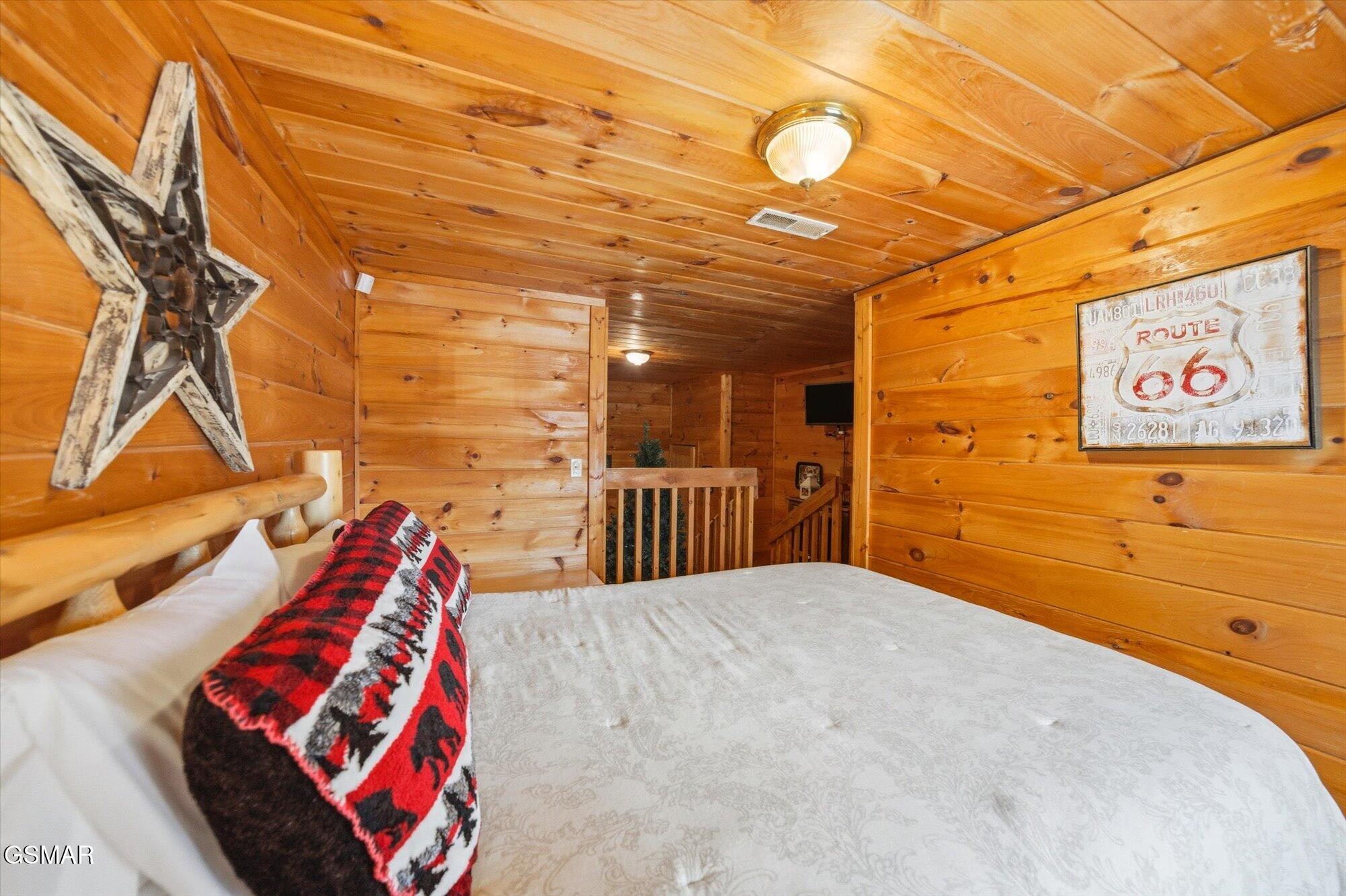Wood-paneled cabin bedroom with a white bed, red patterned blanket, and rustic Route 66 sign.