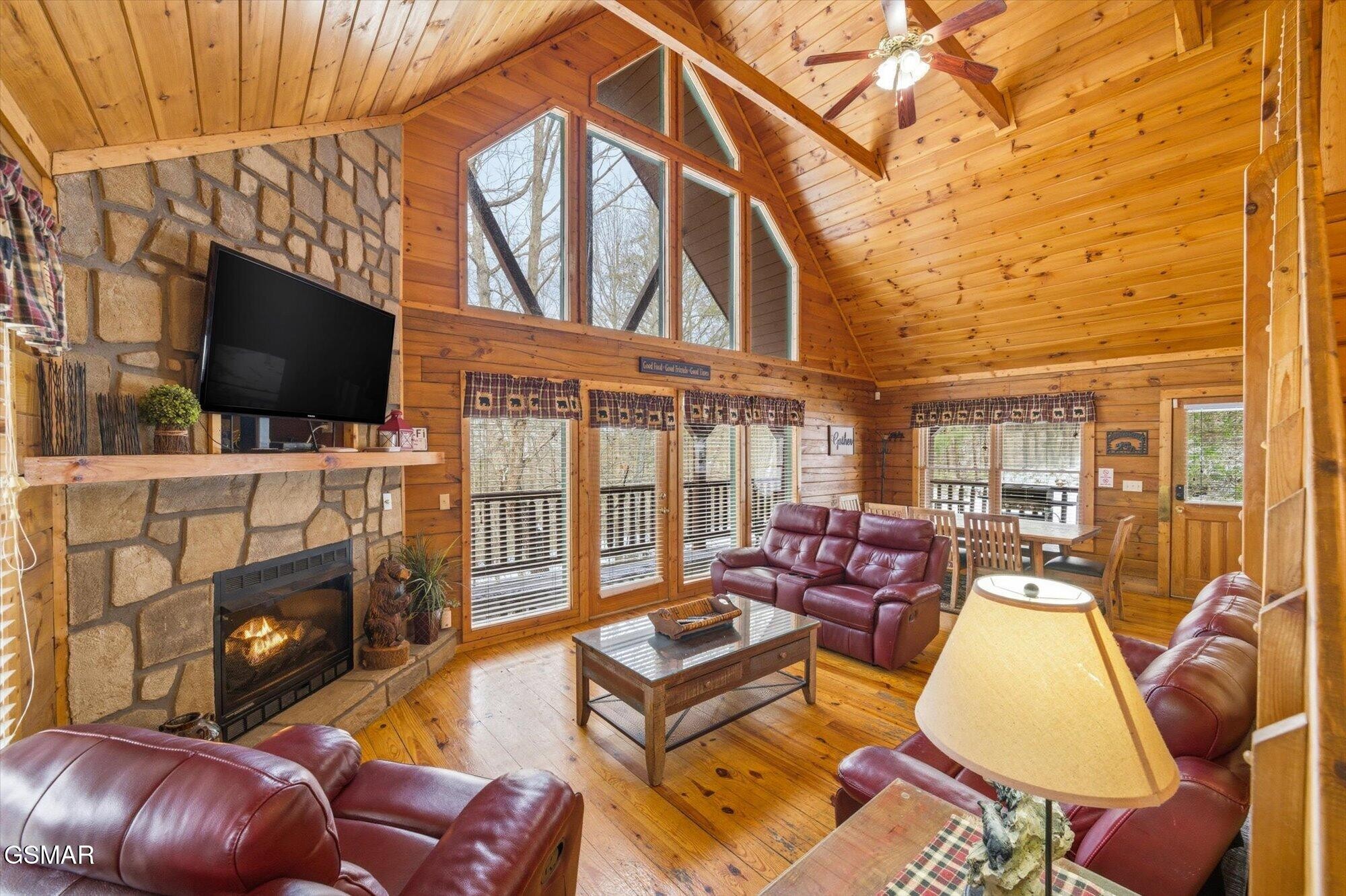 Cabin living room with vaulted wood ceiling, stone fireplace, and burgundy leather seating.