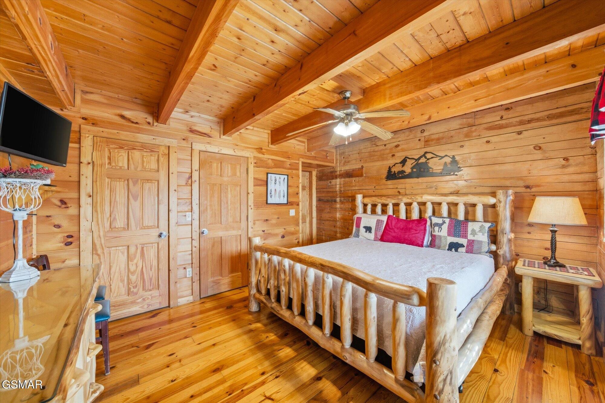 Log cabin bedroom with a rustic log-frame bed, exposed ceiling beams, and honey-colored wood throughout.