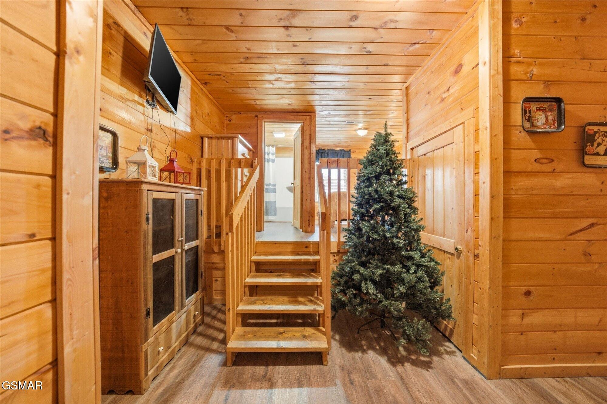 Wood-paneled cabin hallway with stairs and an undecorated Christmas tree.