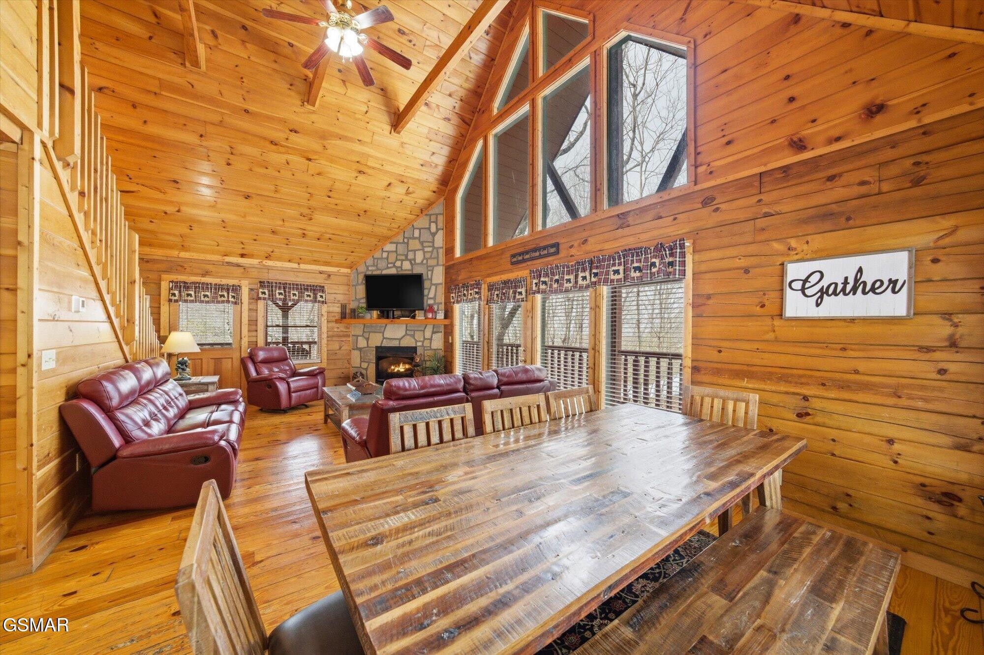 Cabin living and dining room with a vaulted wood ceiling, stone fireplace, and long rustic table.