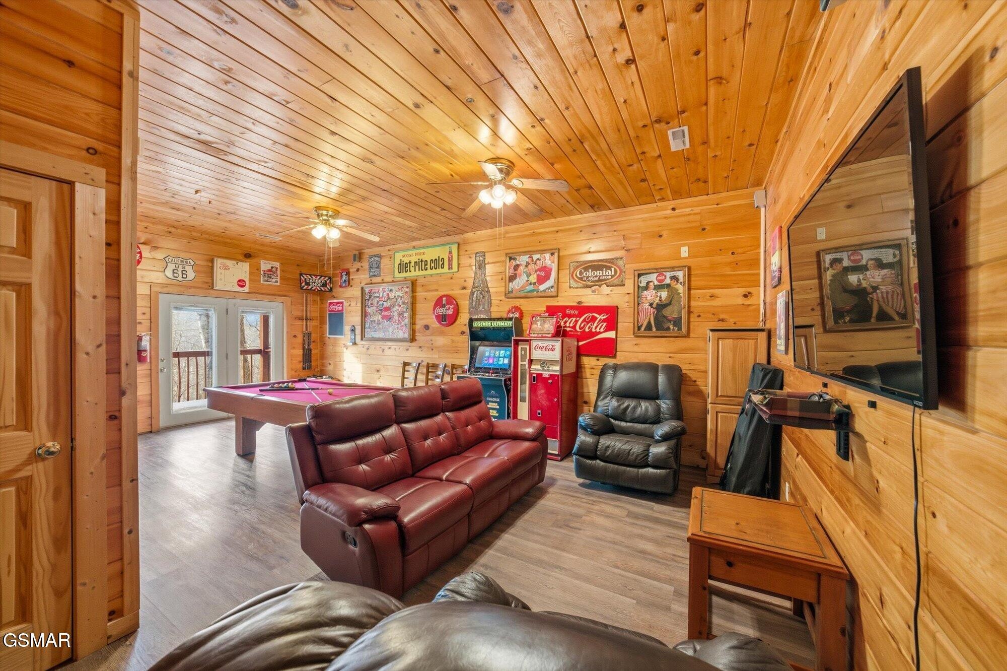 Wood-paneled game room with pool table, leather seating, arcade machine, and wall-mounted television.