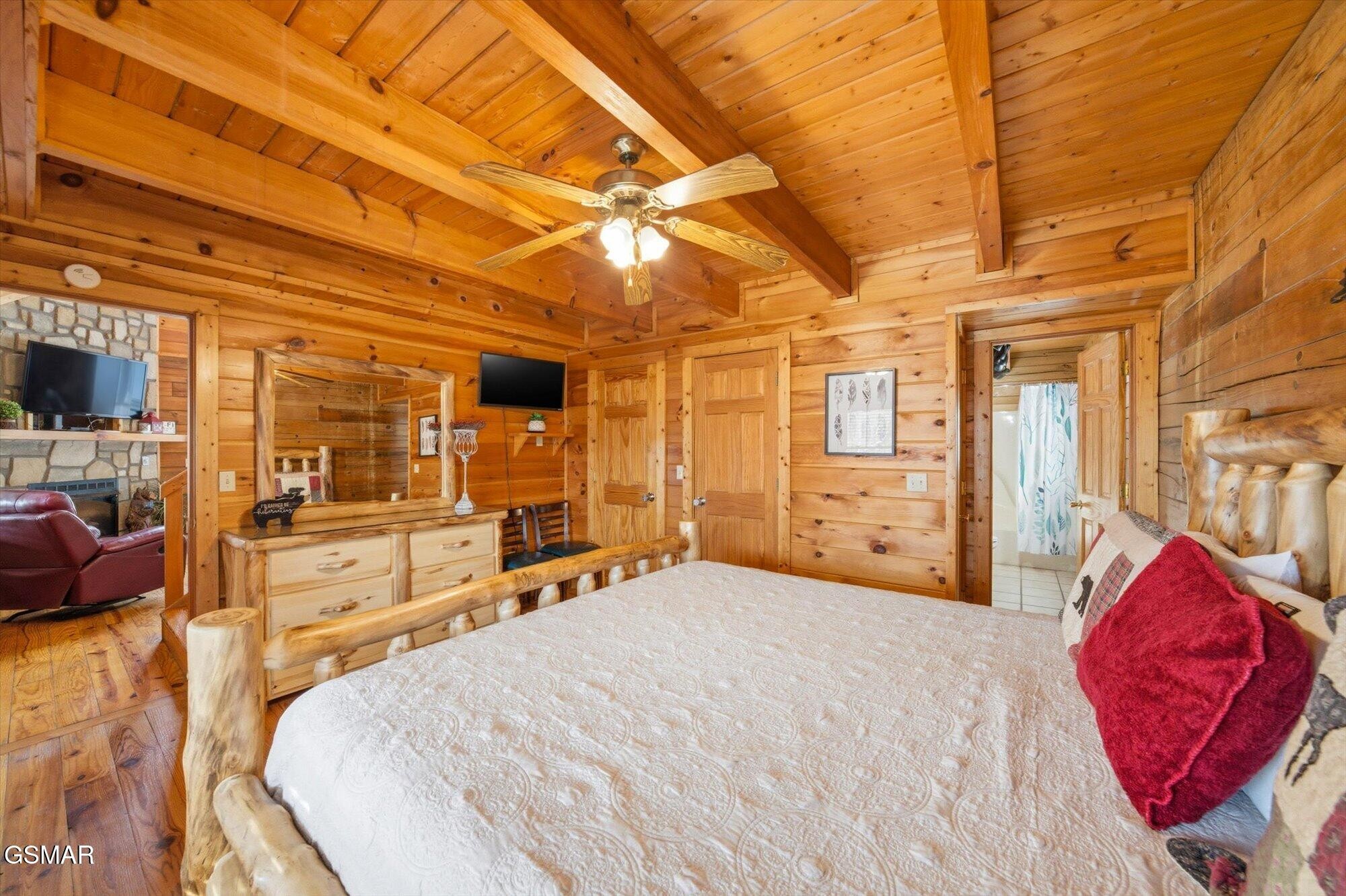 Log-cabin bedroom with a rustic log bed, exposed wood ceiling beams, and a ceiling fan.