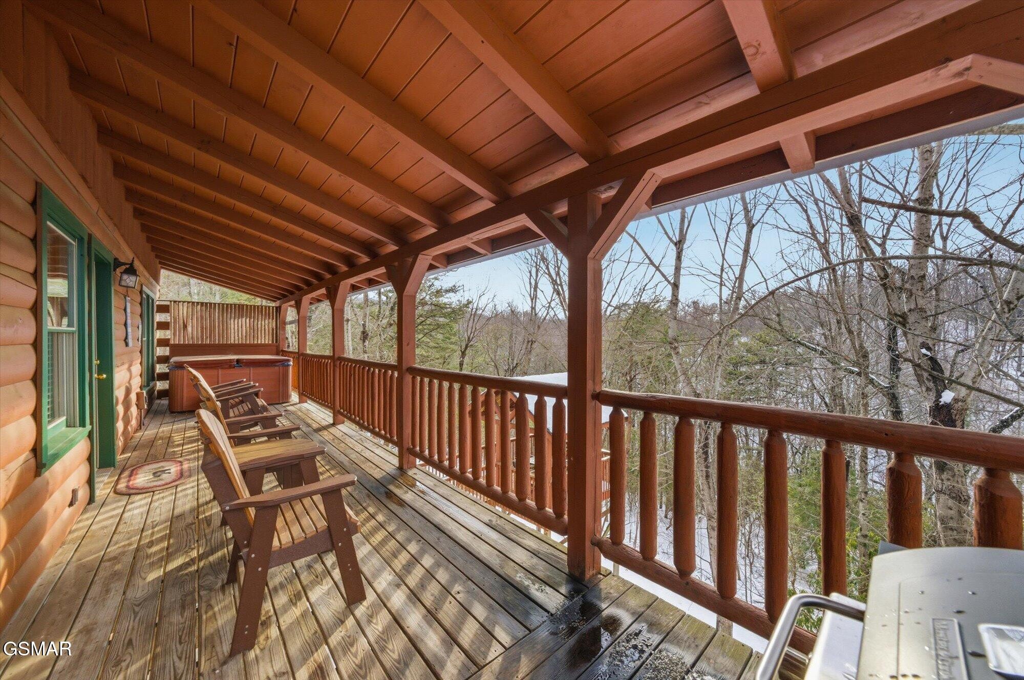 Covered cabin deck with Adirondack chairs and a hot tub overlooking leafless woods.